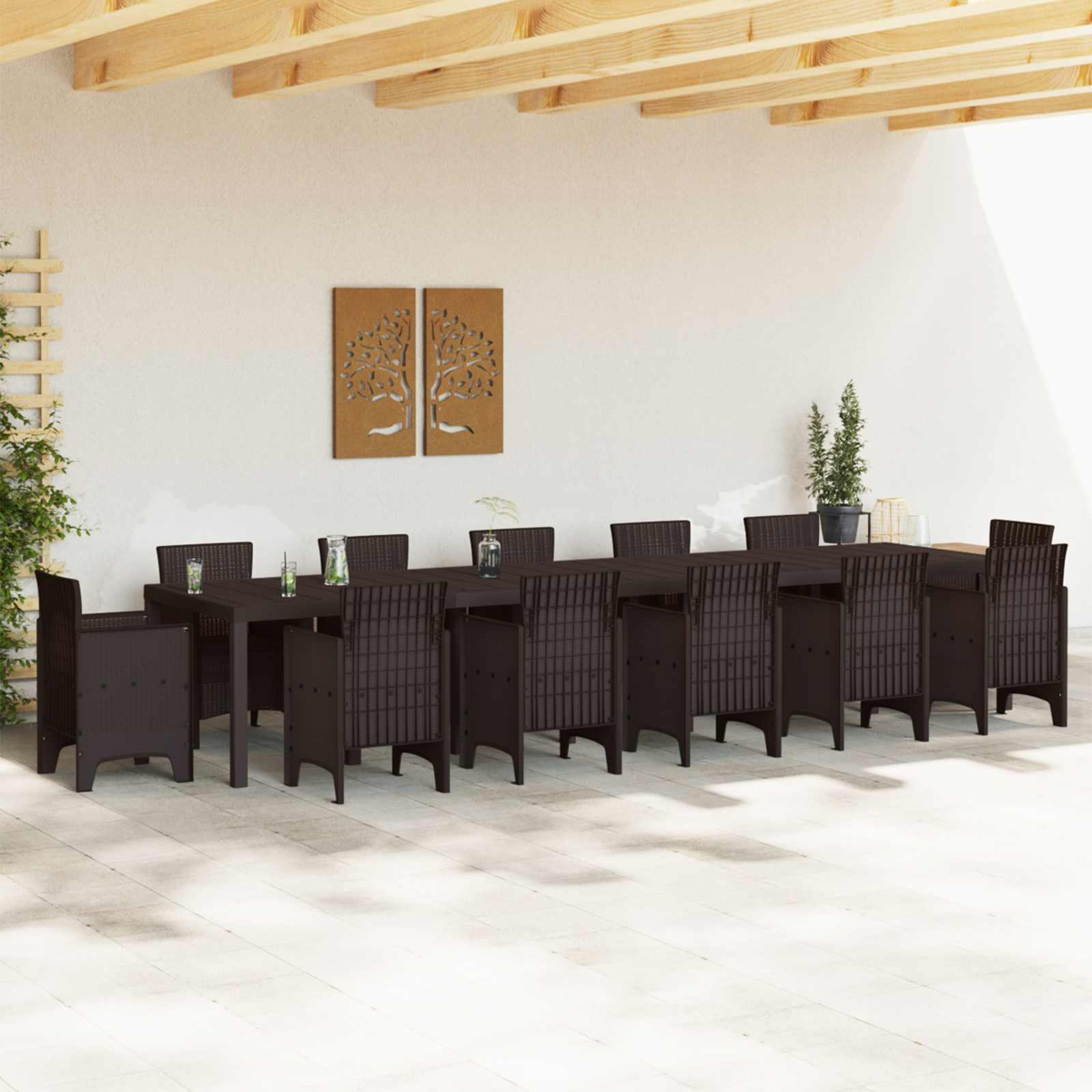 Essgruppe im Freien: ein langer brauner Tisch mit Stühlen. Zwei Baumkunstwerke hängen an einer weißen Wand. Holzträger darüber.