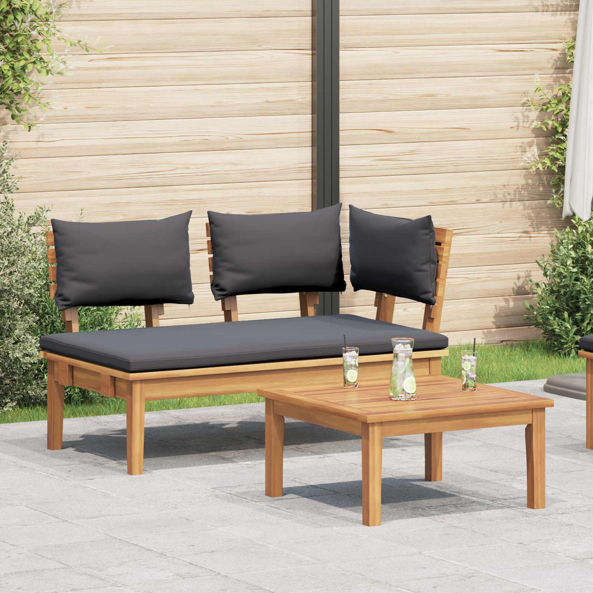 Holzbank mit grauen Kissen, kleiner Tisch mit Getränken, in einer Terrasse mit Holzzaun im Hintergrund.