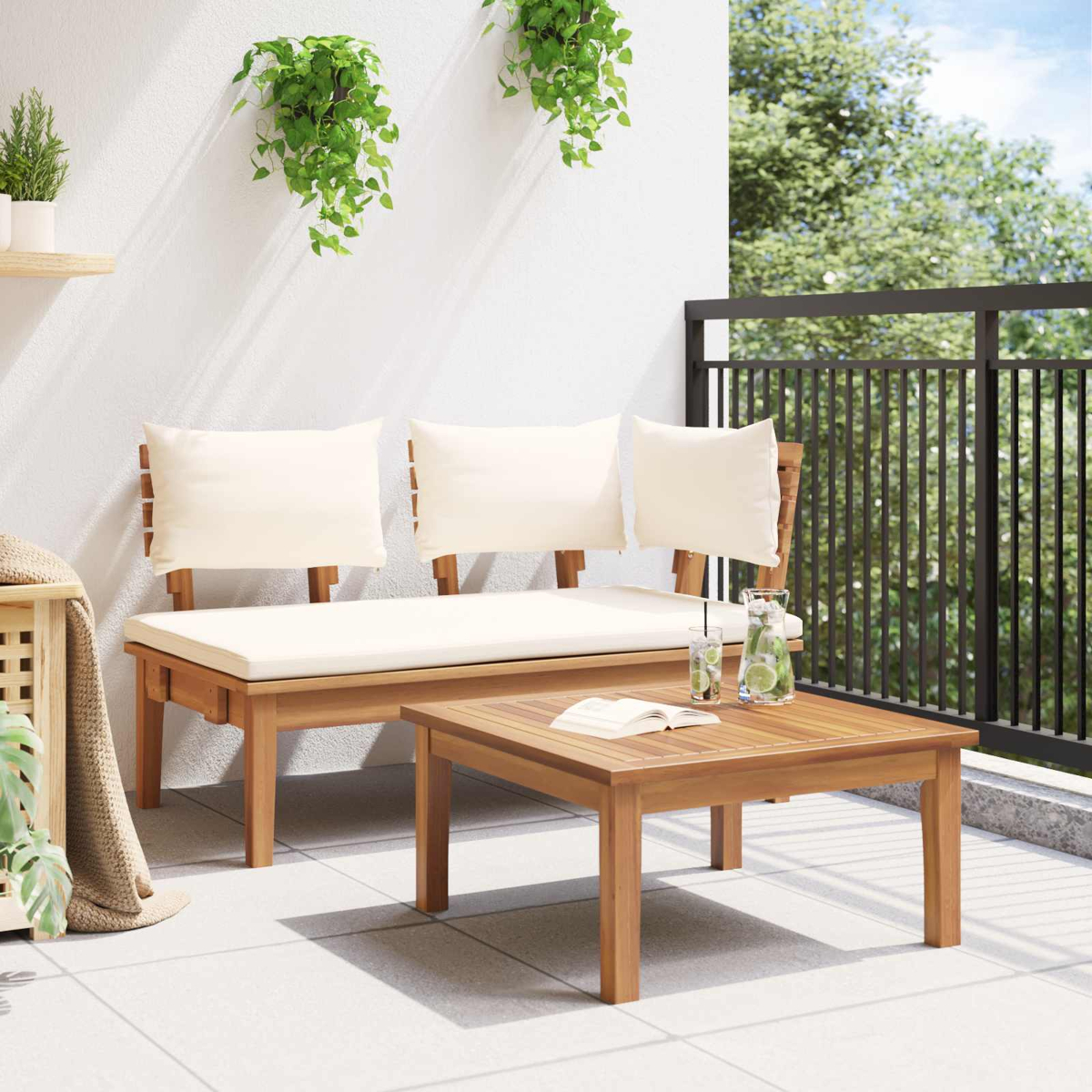 Balkon mit Holzbank und Tisch. Weiße Kissen, hängende Pflanzen, Gläser mit Getränken und ein Buch. Im Hintergrund ein Baum.
