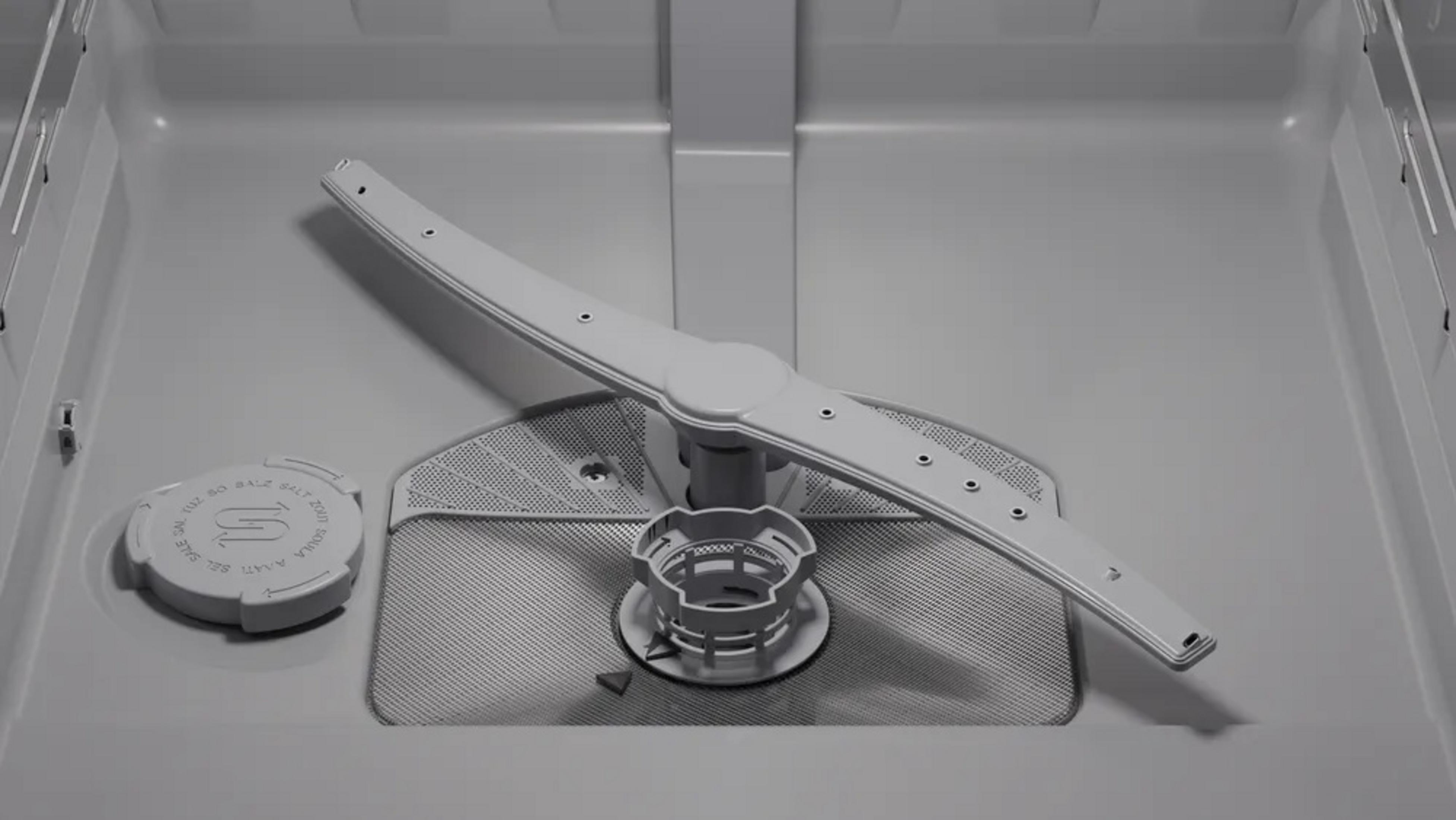 Wnętrze zmywarki. Na środku białe ramię natryskowe. Na dole pojemnik na sól i filtr.