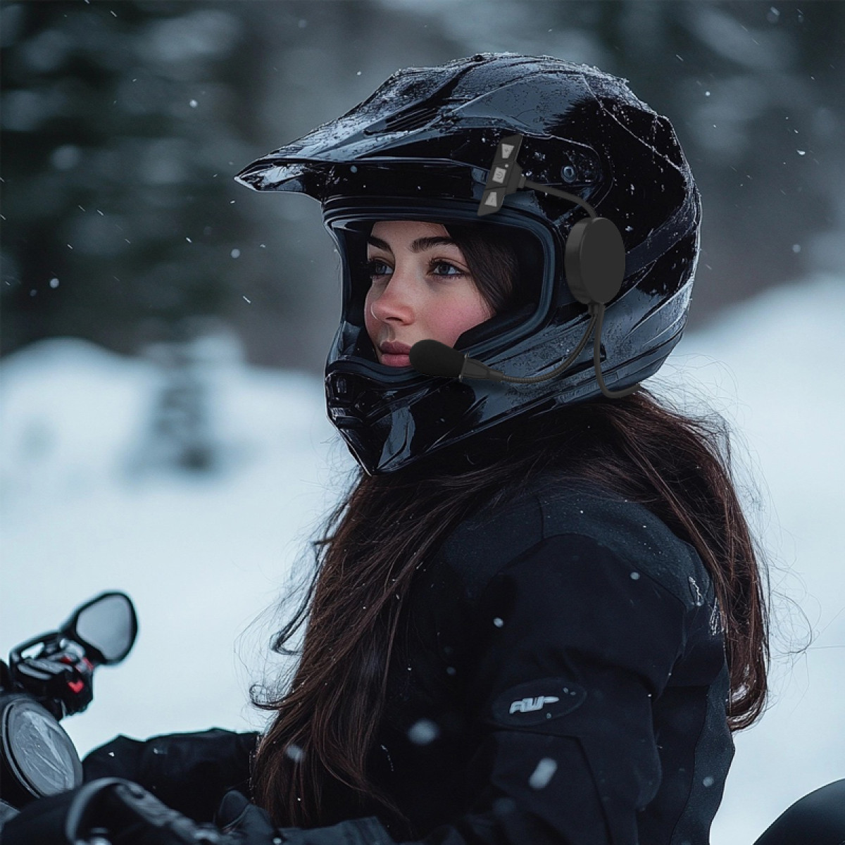Frau mit schwarzem Helm und Kommunikationsgerät auf einem Schneemobil in verschneiter Umgebung. Dunkle Jacke und lange Haare.