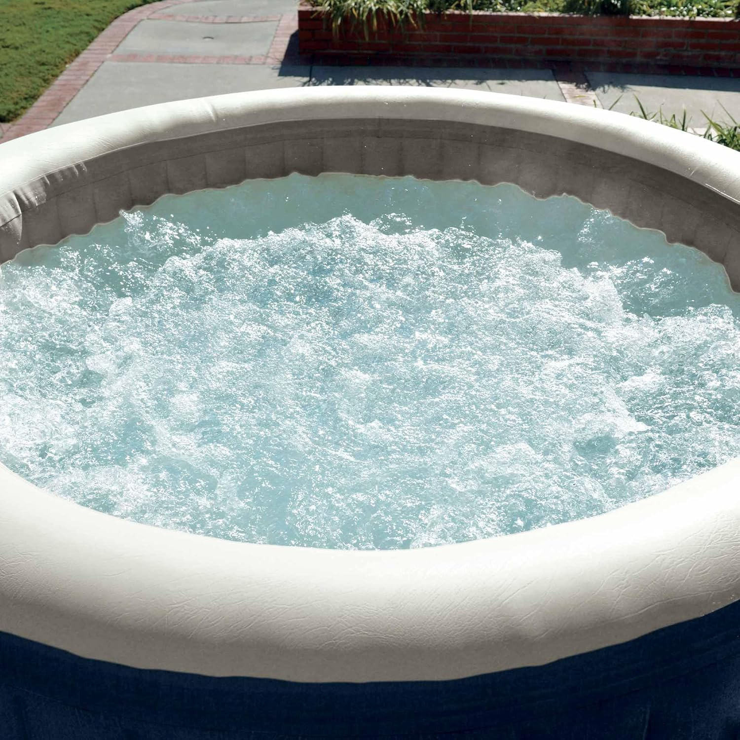 Ein aufblasbarer Whirlpool mit sprudelndem Wasser. Die Wanne ist blau, weiß und grau und steht auf einer Terrasse mit Backsteinmauer.