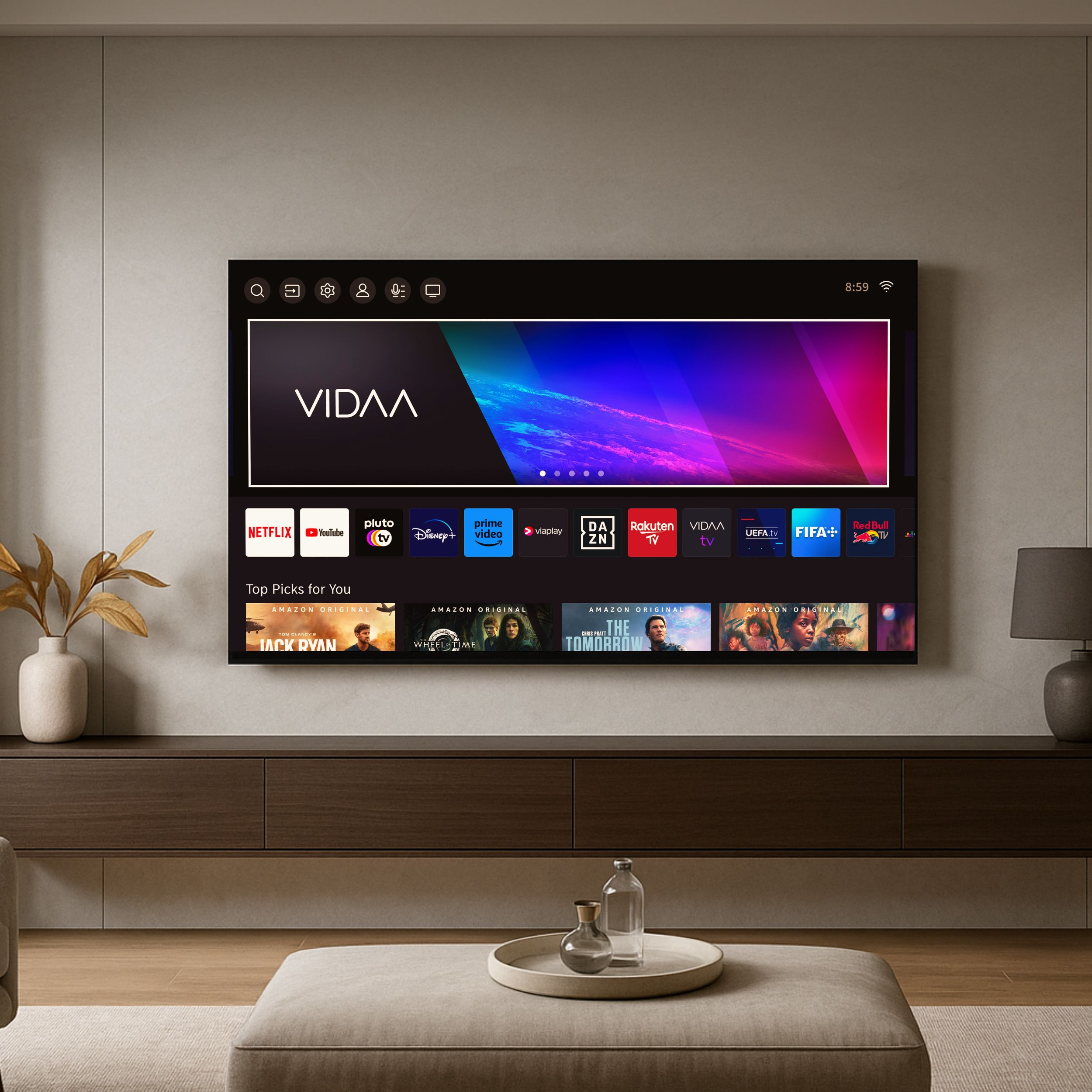 Ein Fernseher zeigt einen Streaming-Dienst. Es gibt eine Vase mit Trockenblumen. Ein Tisch mit Dekoration und eine Fußstütze.
