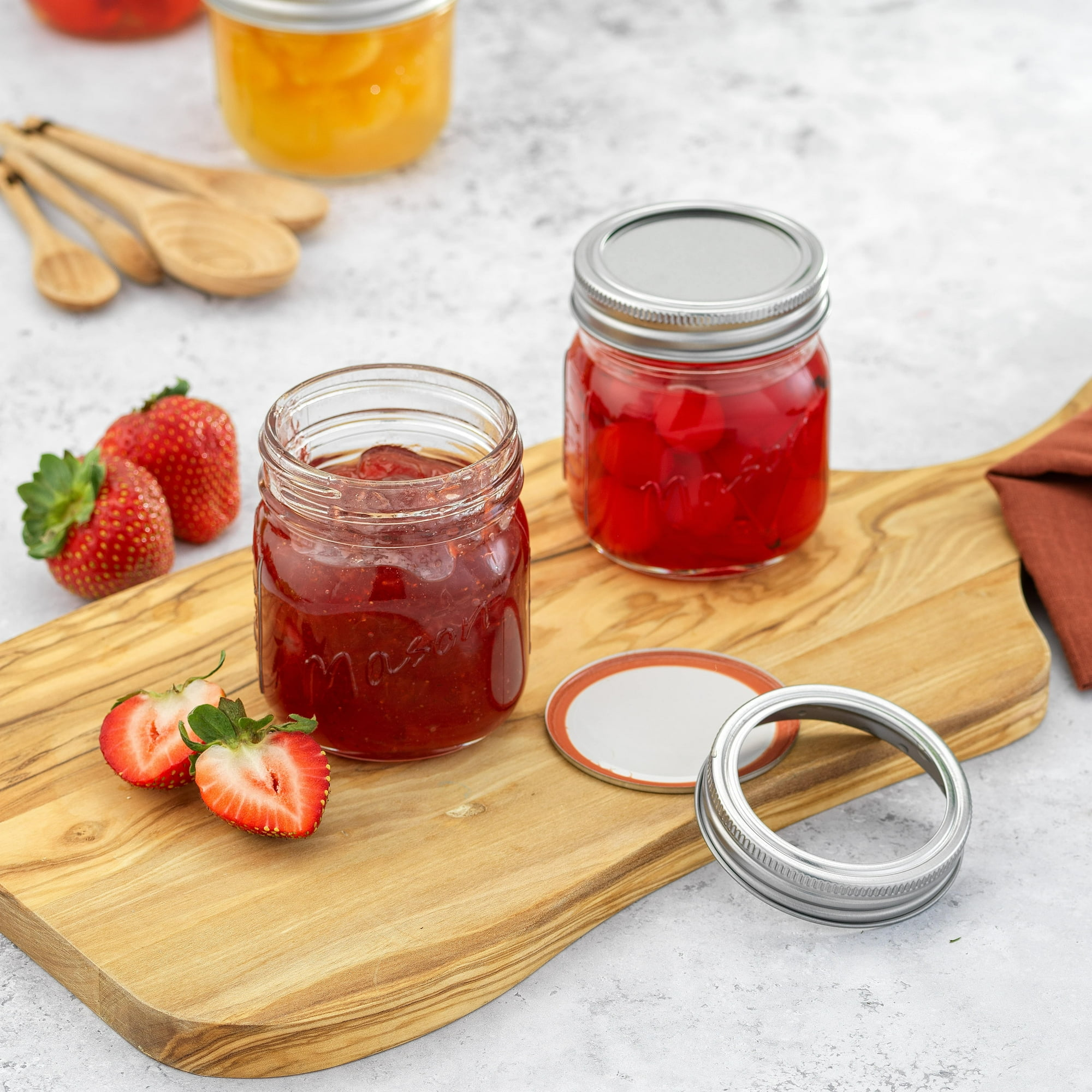 Gläser mit Marmelade und Konserven auf einem Holzbrett mit Erdbeeren und Löffeln.