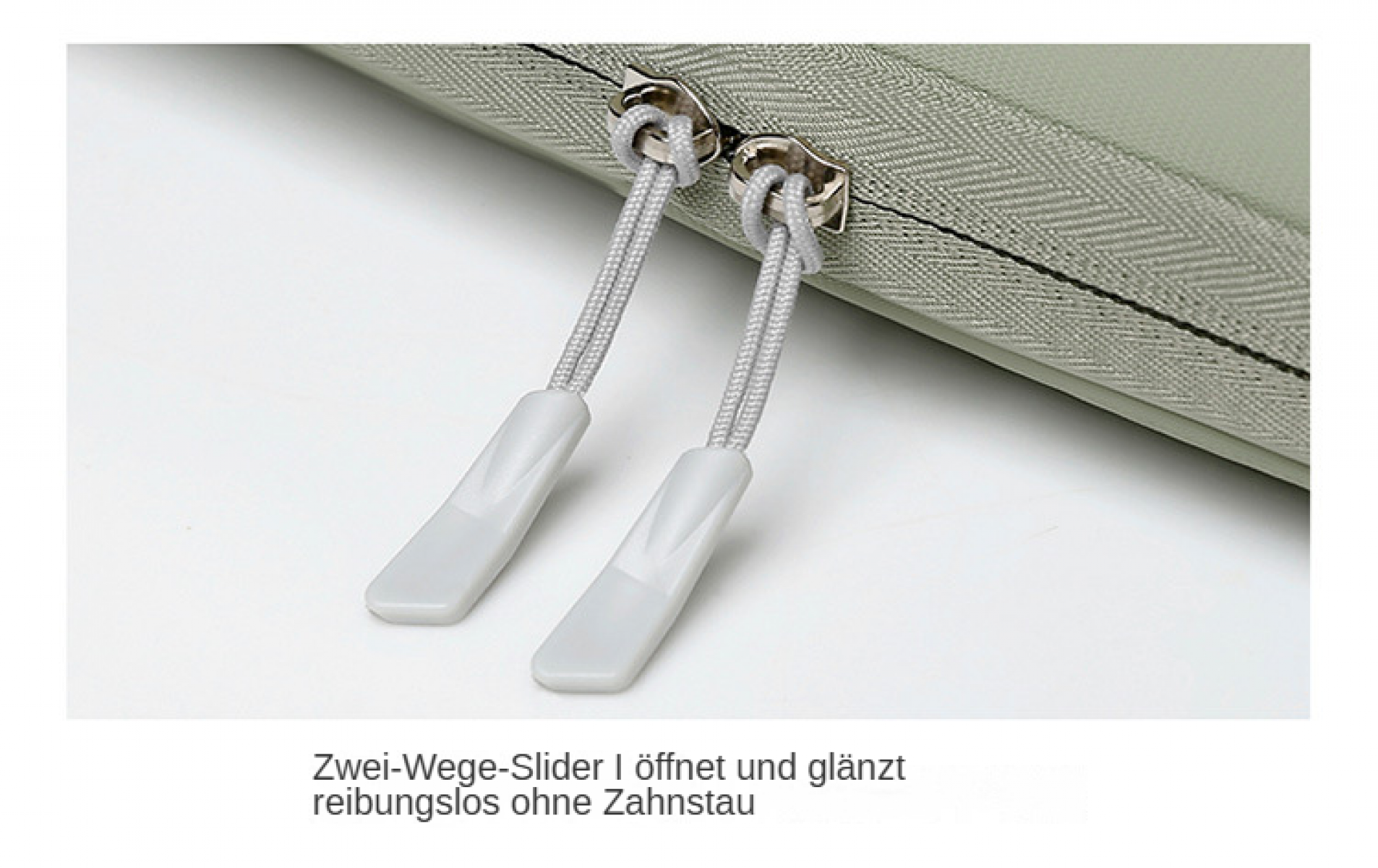 Nahaufnahme eines Reißverschlusses mit zwei weißen Zuglaschen. Der Reißverschluss befindet sich auf einem hellgrünen Stoff. Weißer Hintergrund.