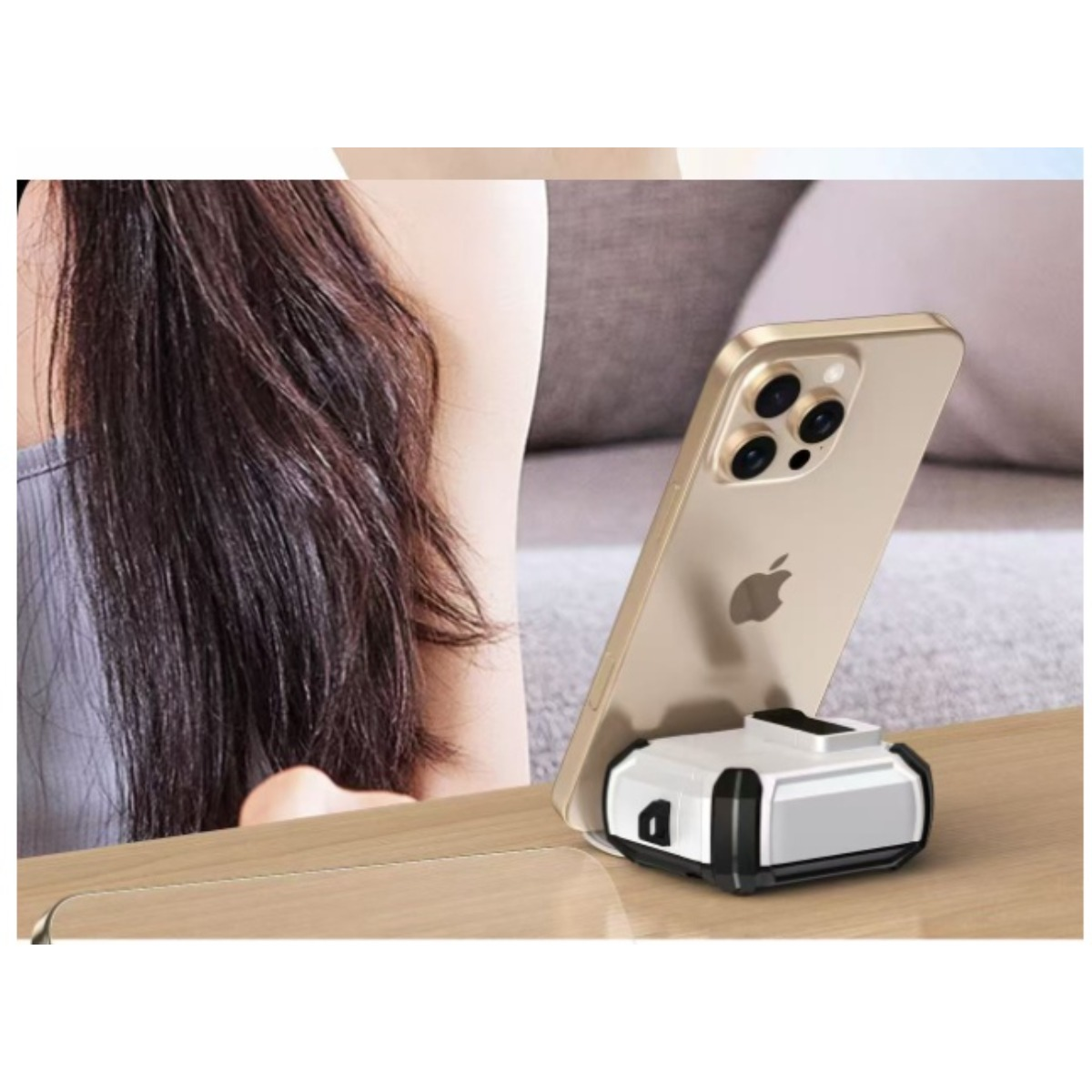 Ein goldenes iPhone steht auf einer weißen und schwarzen Ladestation auf einer Holzoberfläche. Im Hintergrund ist eine Person.