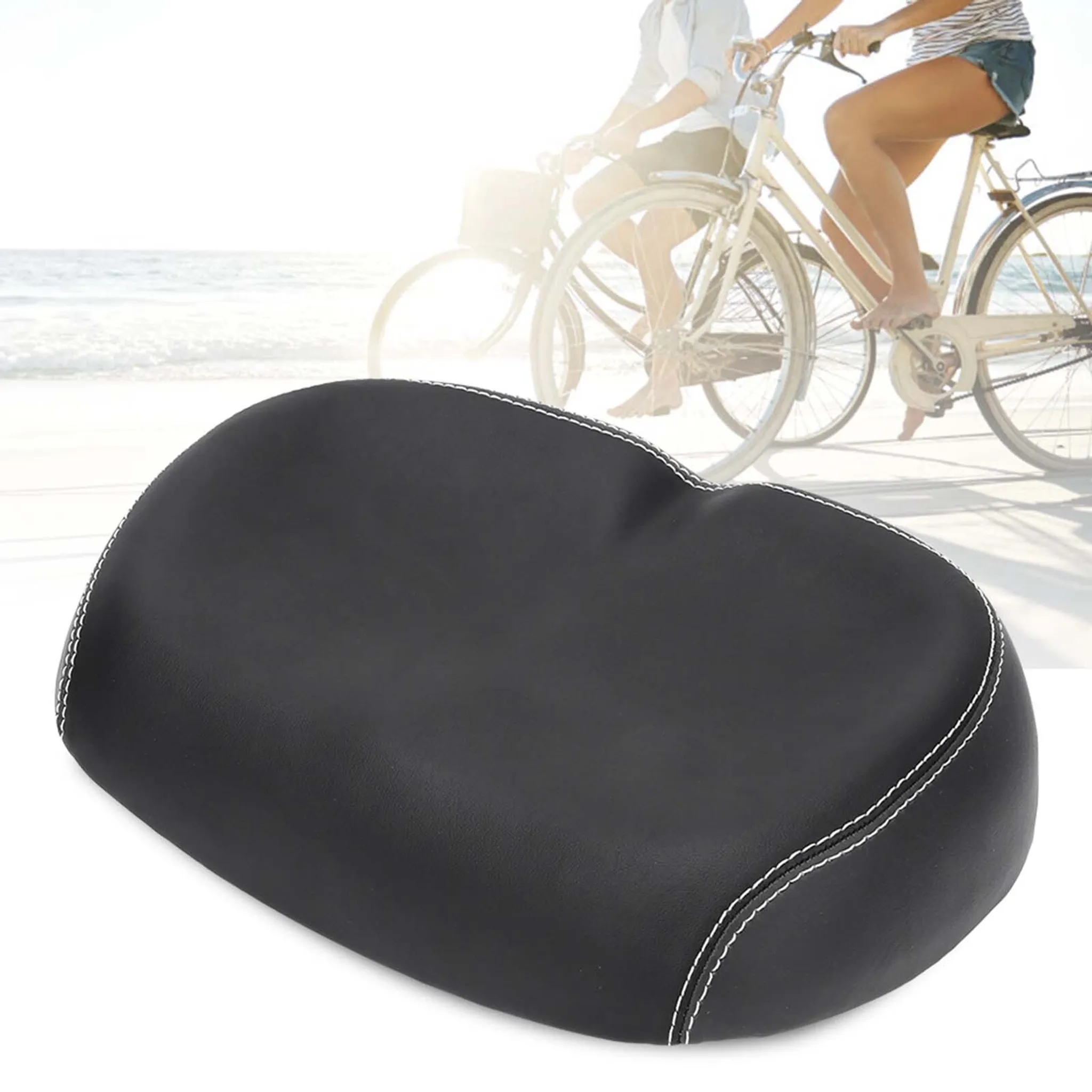 Schwarzer Fahrradsitz mit weißen Nähten im Vordergrund. Zwei Personen fahren im Hintergrund mit dem Fahrrad am Strand.