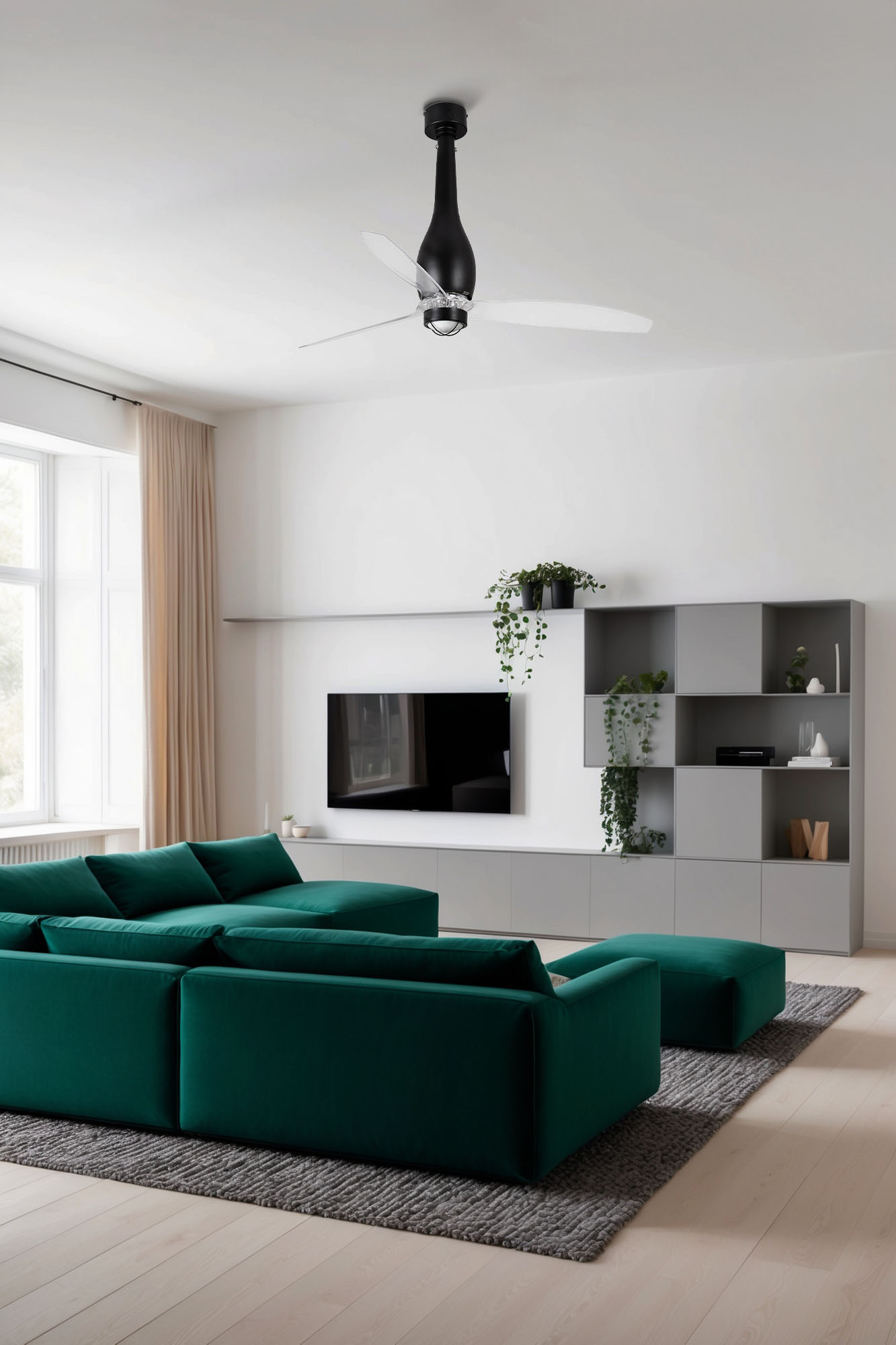 Soggiorno con divano verde, tappeto grigio e ventilatore a soffitto. TV a muro, piante e finestra con tende.