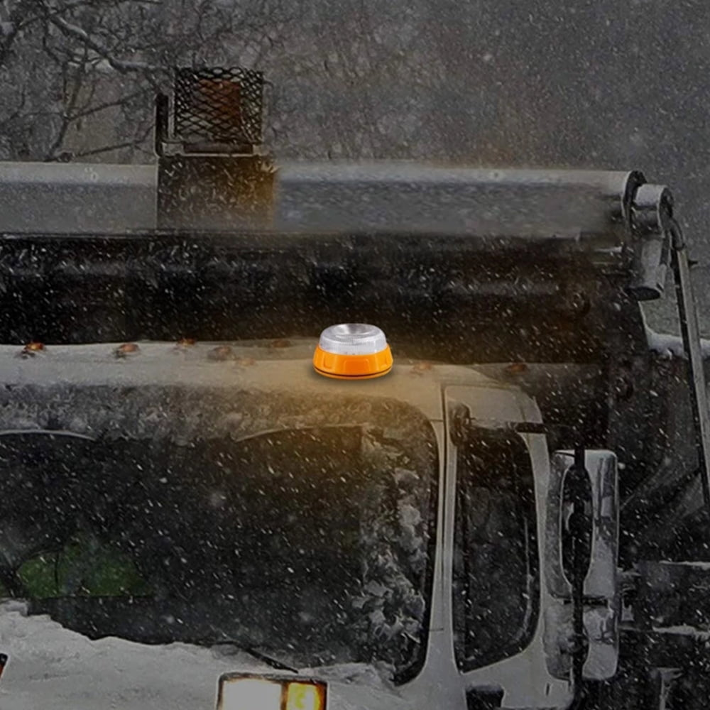 Ein orange-silbernes Licht sitzt auf dem Dach eines Fahrzeugs. Schnee fällt. Die Szene spielt sich im Freien ab, wahrscheinlich im Winter.
