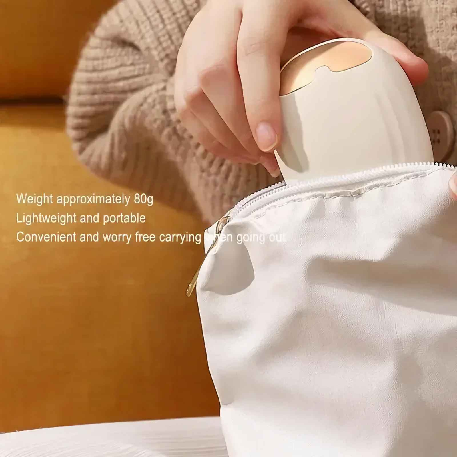 Eine Hand legt ein cremefarbenes Gerät in eine weiße Tasche. Eine Person trägt einen braunen Pullover.