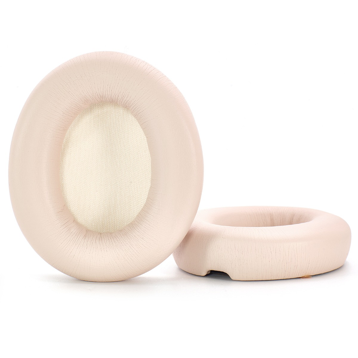 Dos almohadillas beige para auriculares sobre una superficie blanca. Una está en posición vertical, la otra está acostada. Ambas tienen un centro color crema.