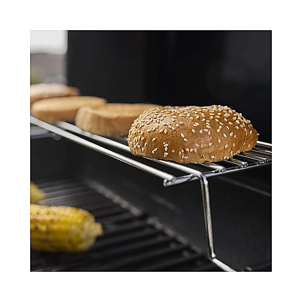 Primo piano di una griglia con panini per hamburger su una griglia. Il panino superiore è ricoperto di semi di sesamo. È visibile anche il mais.