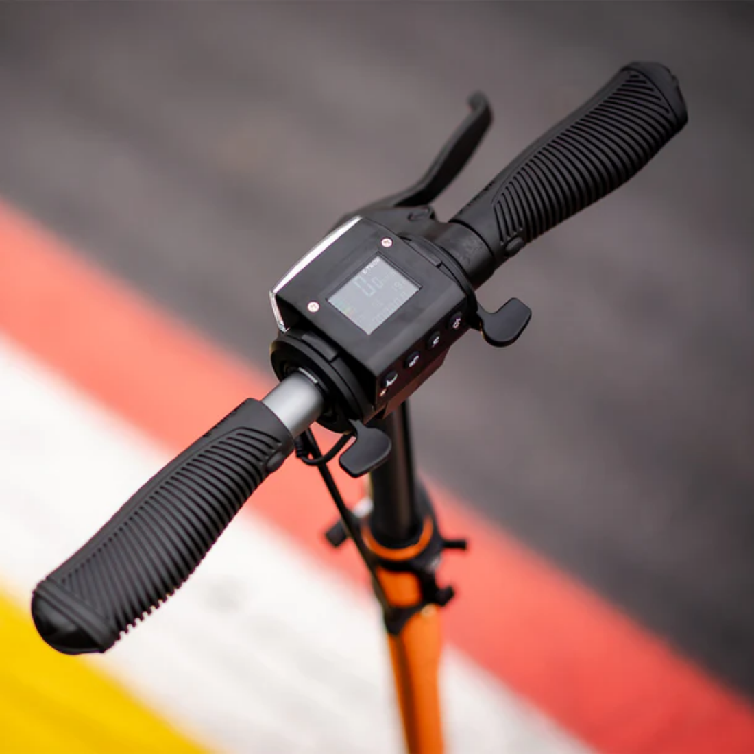 Zbliżenie kierownicy hulajnogi elektrycznej. Czarne uchwyty, wyświetlacz i elementy sterujące. Pomarańczowy trzon. Tło z czerwonymi, żółtymi i szarymi liniami.