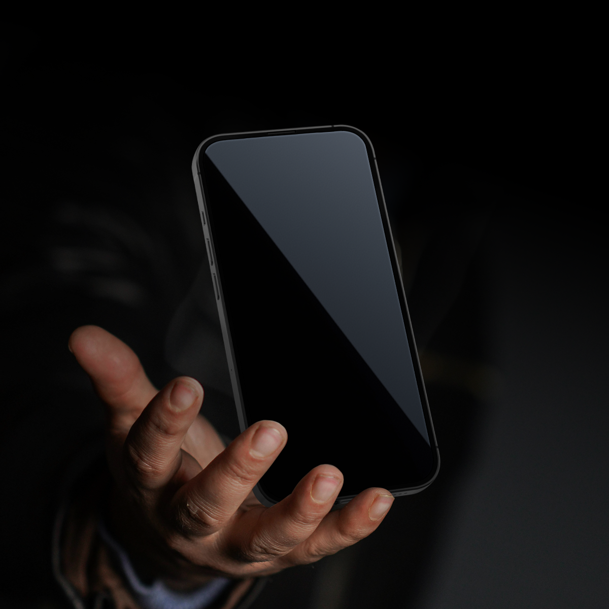 Ręka trzyma czarny smartfon na ciemnym tle. Ekran odbija światło. Telefon jest w centrum uwagi na zdjęciu.