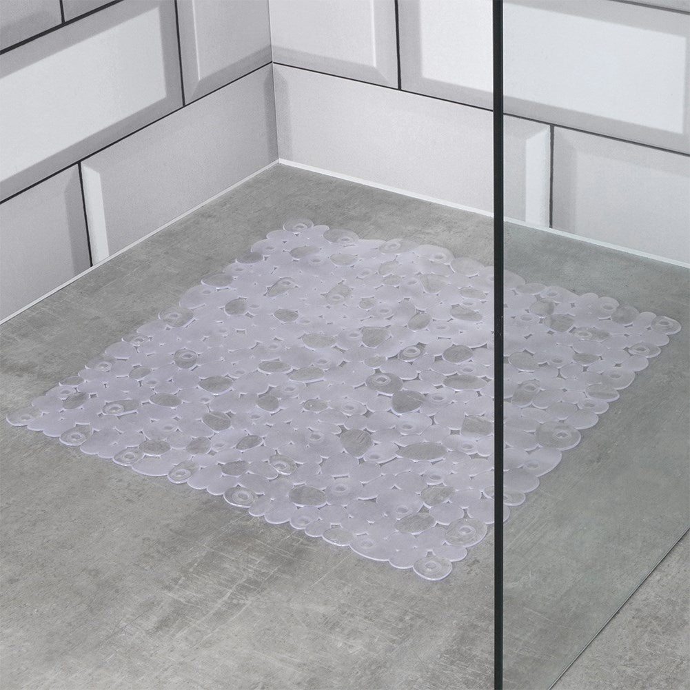 Una alfombra de baño transparente y texturizada sobre un suelo de baldosas grises. Azulejos blancos rectangulares forman las paredes de la ducha.