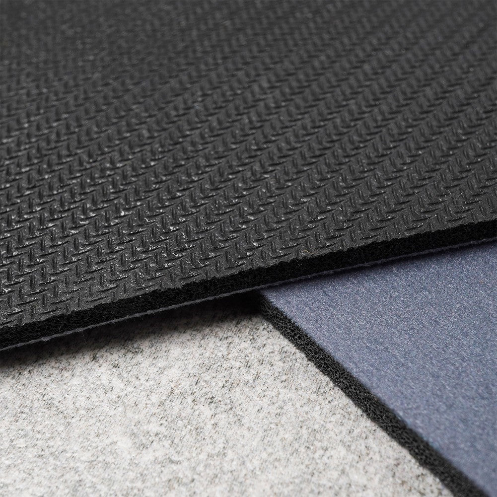 Primer plano de tres capas de alfombras. La superior es negra texturizada, la del medio azul, la inferior gris. Los bordes muestran las capas.