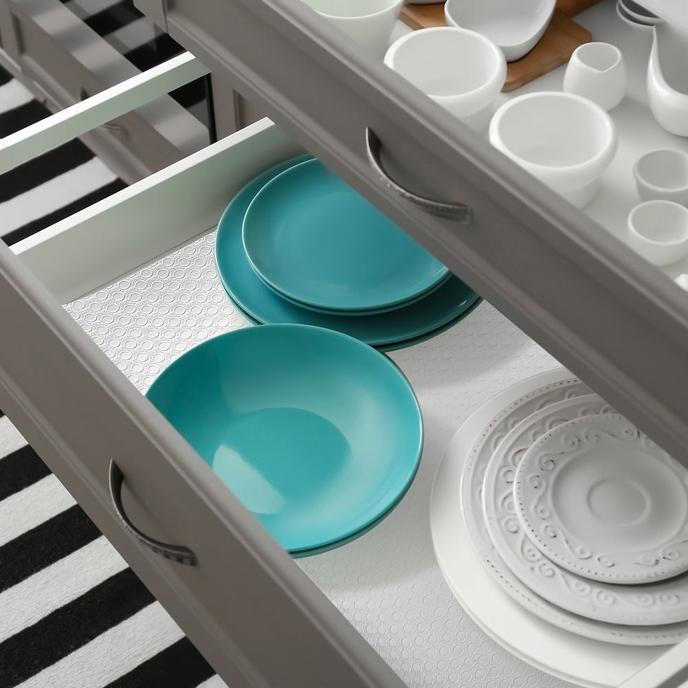 Cajón de cocina abierto con platos turquesa y platos blancos. Una alfombra a rayas blancas y negras está en el fondo.