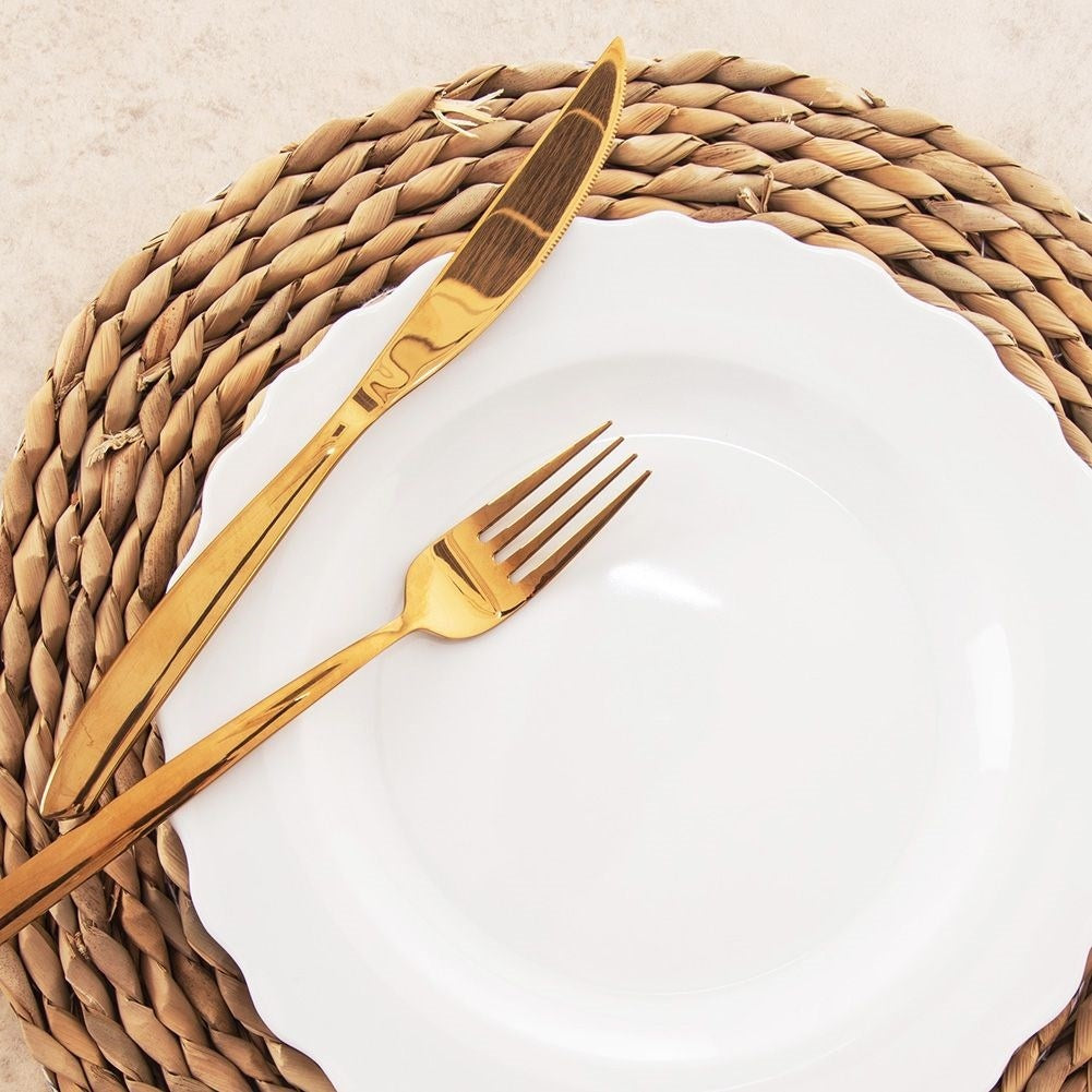 Un plato blanco con utensilios dorados (cuchillo y tenedor) sobre un mantel individual tejido. El fondo es beige.