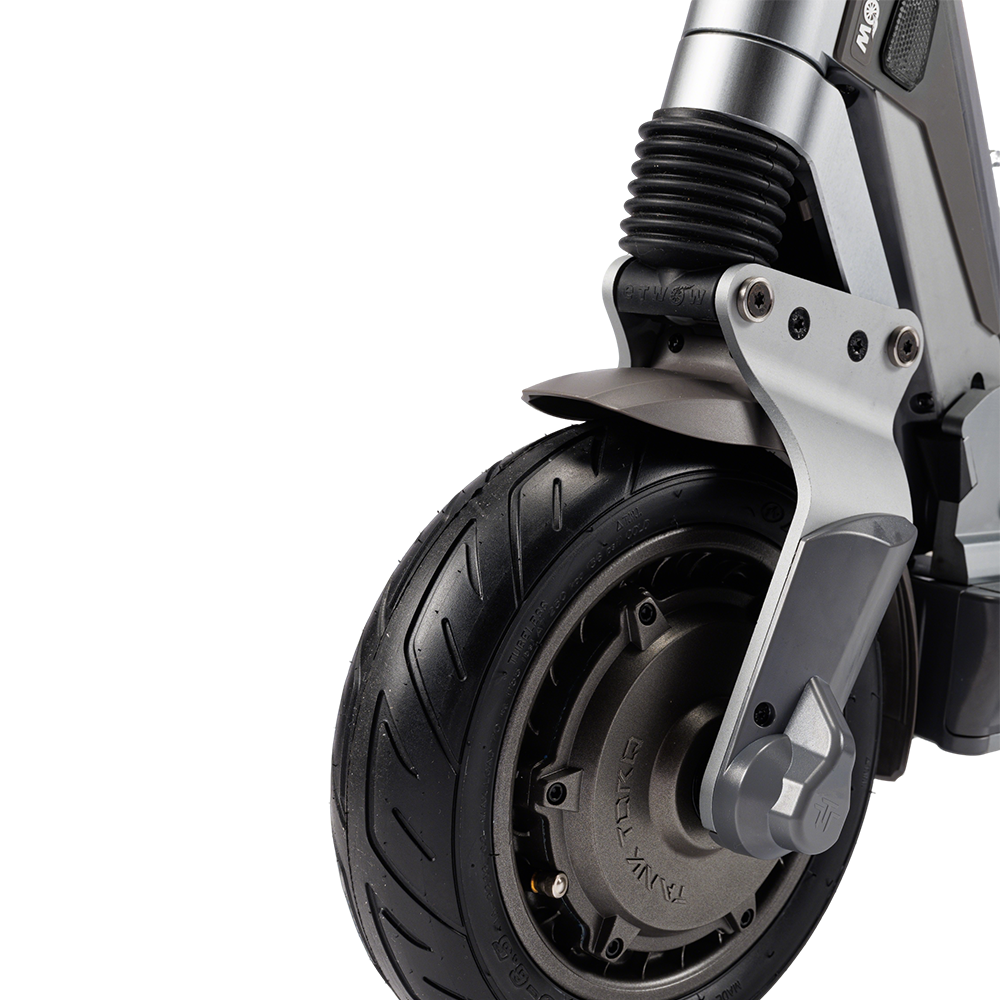 Zbliżenie przedniego koła hulajnogi elektrycznej. Opona jest czarna. Metalowa szara rama, zawieszenie i błotnik. Białe tło.