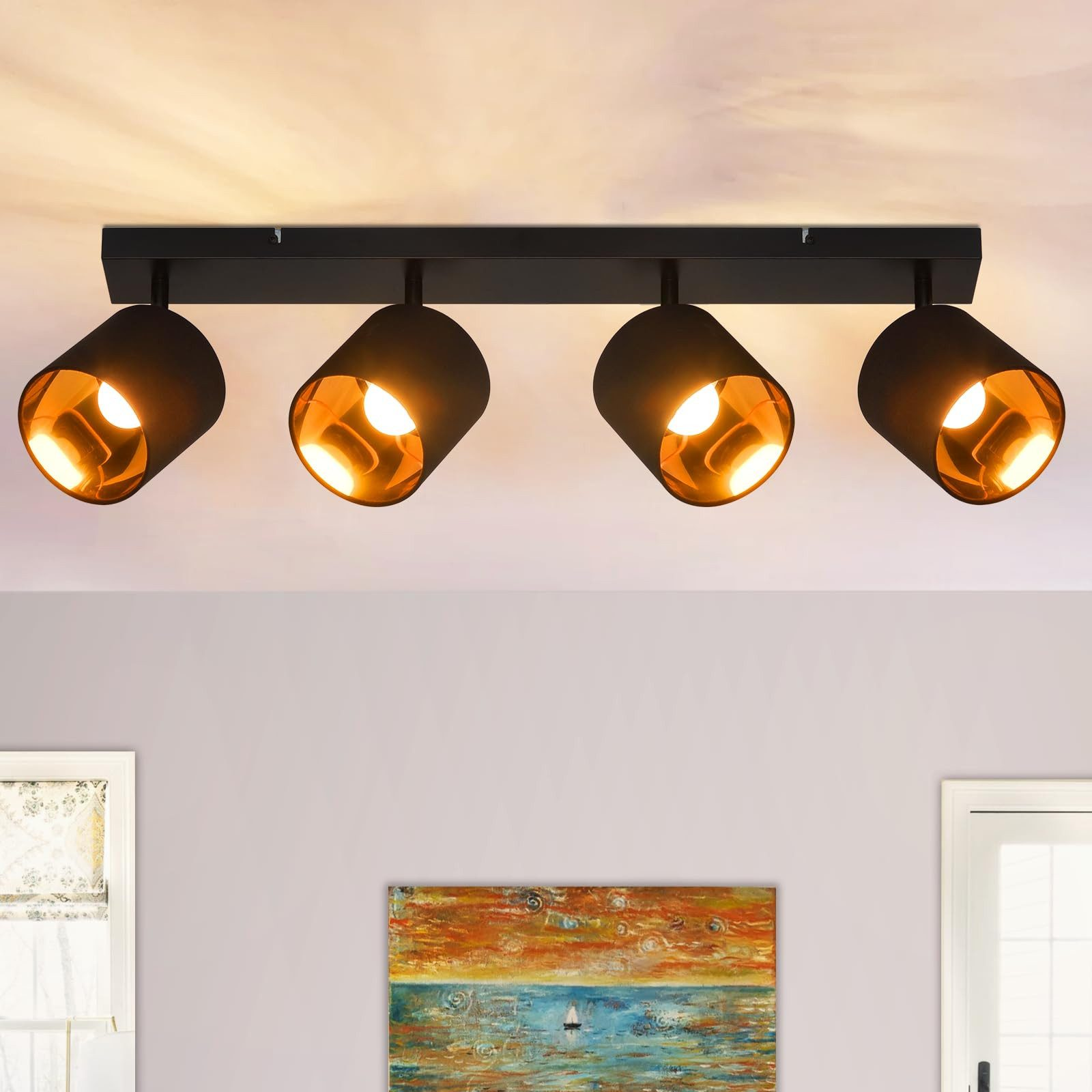 Quattro faretti neri a soffitto. Sotto c'è un dipinto e una finestra. La luce è accesa.