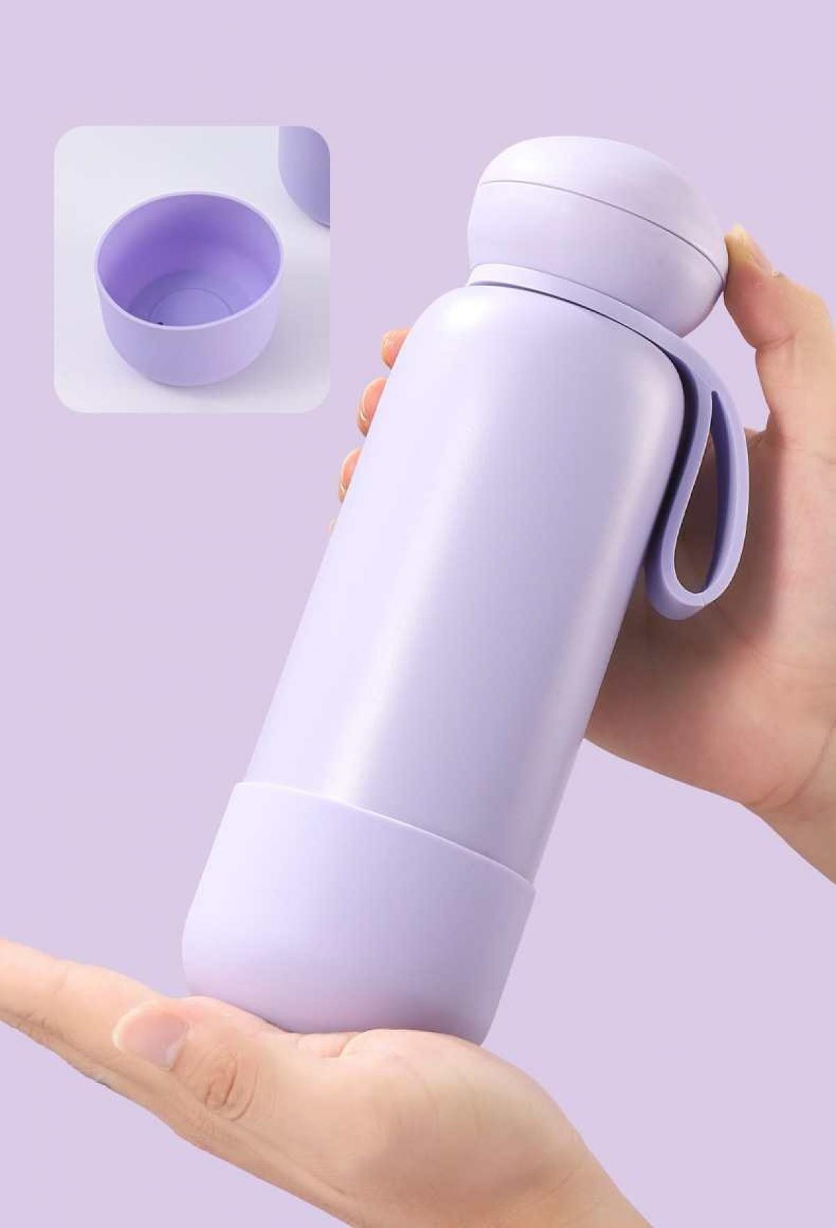 Eine Hand hält eine lavendelfarbene Wasserflasche. Ein kleiner Becher und eine weitere Flasche befinden sich im Hintergrund.