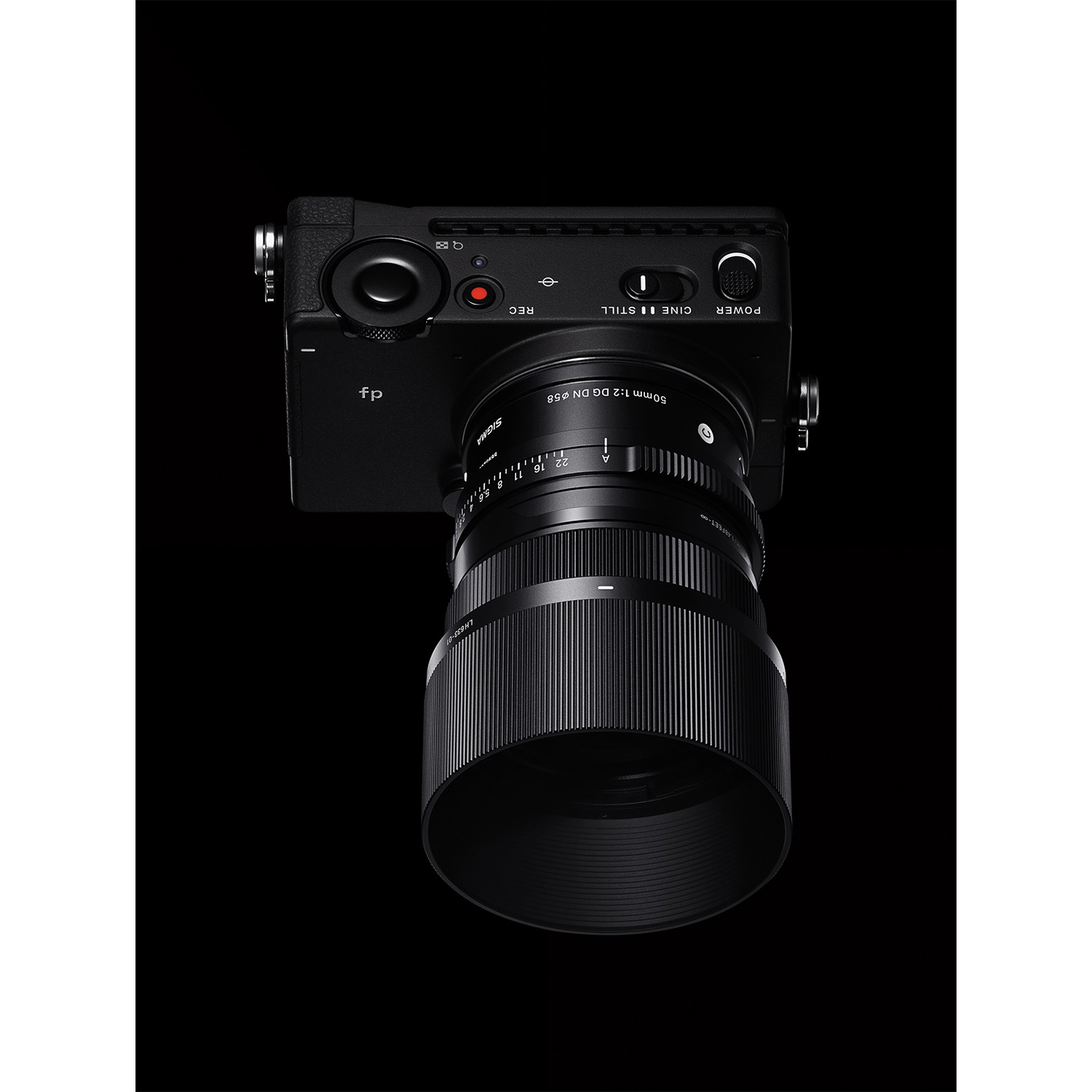 Una fotocamera Sigma fp nera con un obiettivo da 50 mm è centrata su sfondo nero. Sono visibili dettagli come le marcature dell'obiettivo.