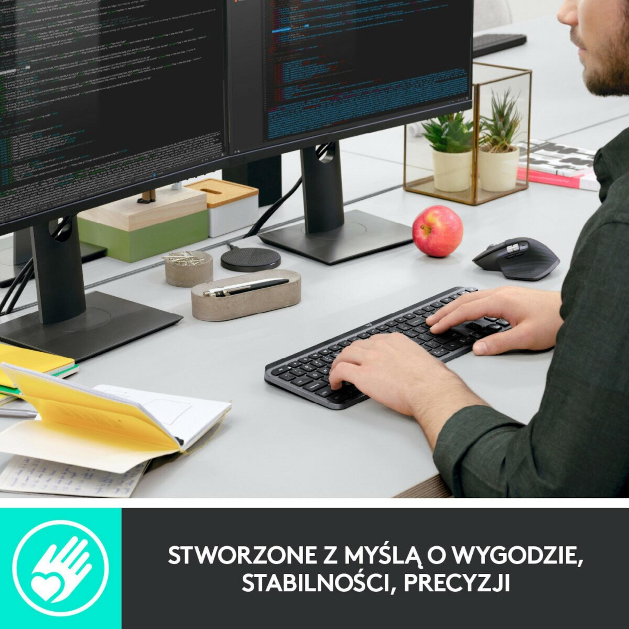 Osoba używa klawiatury z dwoma monitorami wyświetlającymi kod. Jabłko i mysz są na biurku.