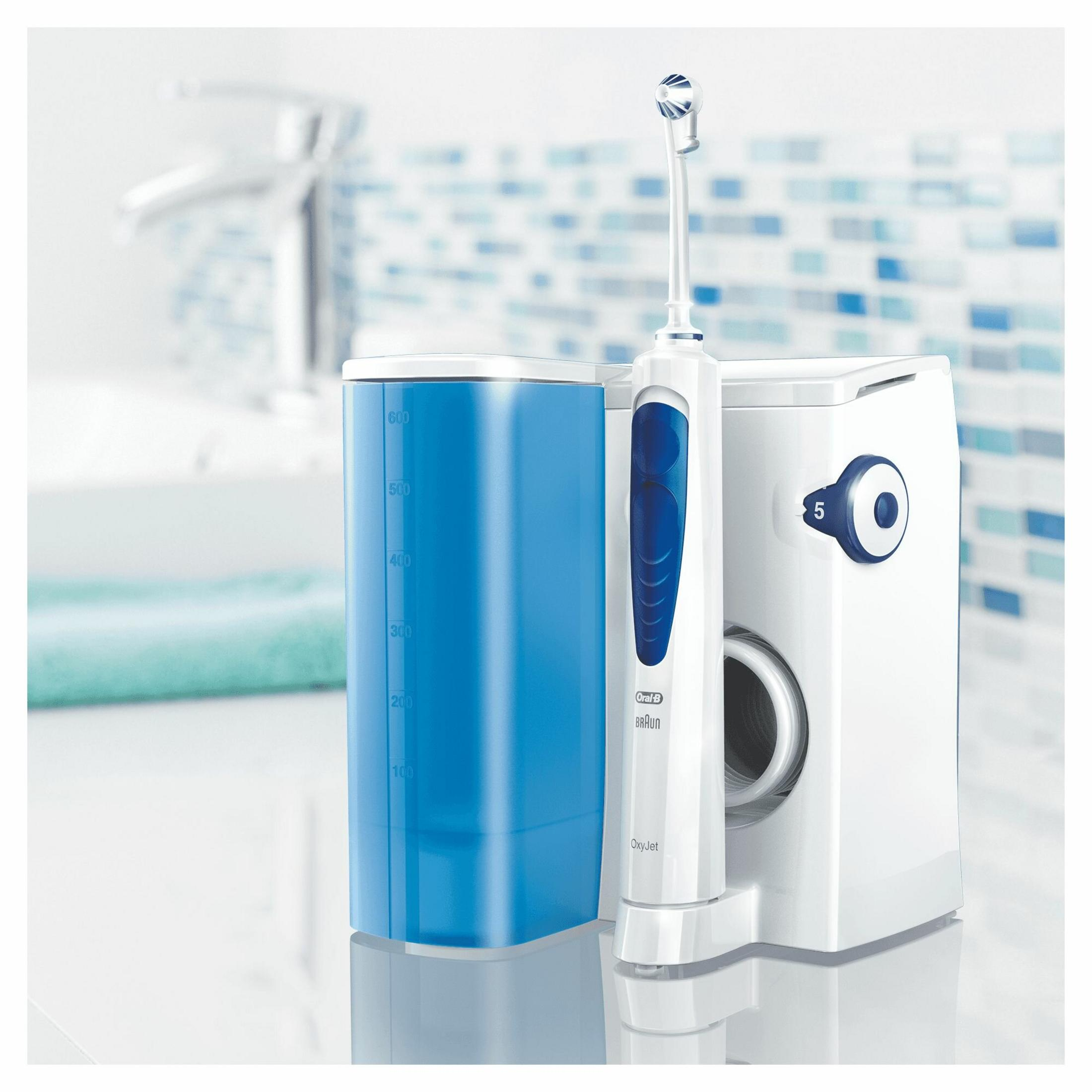 Un idropulsore Oral-B Braun OxyJet bianco e blu.  È posizionato su una superficie bianca con un contenitore d'acqua blu.