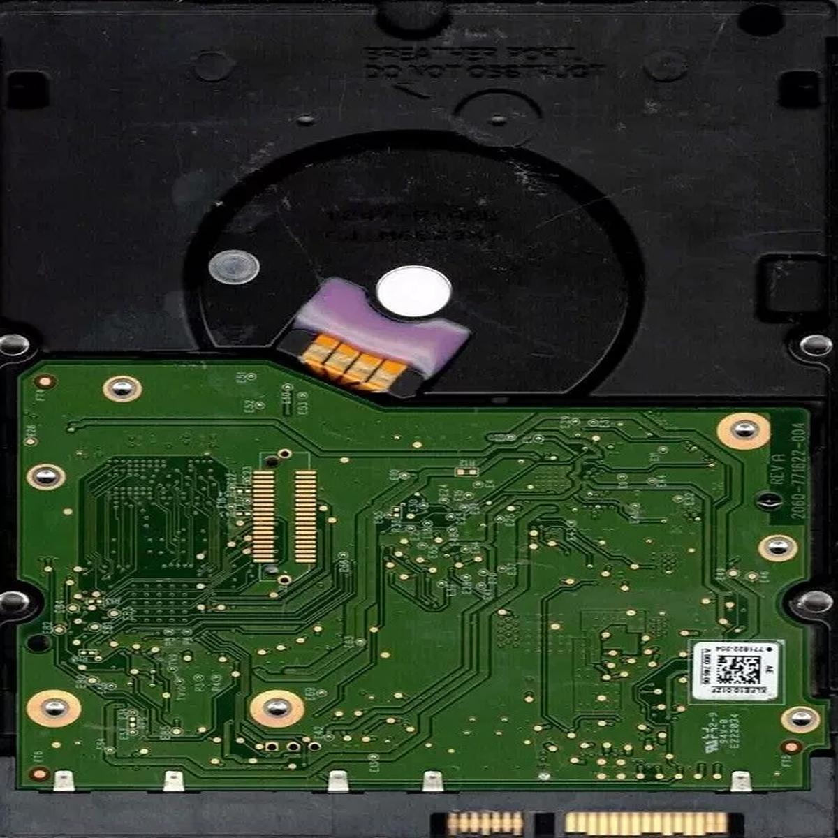 Sono visibili i componenti interni di un disco rigido. Una scheda a circuito verde con connettori dorati si trova sotto una sezione nera, circolare.