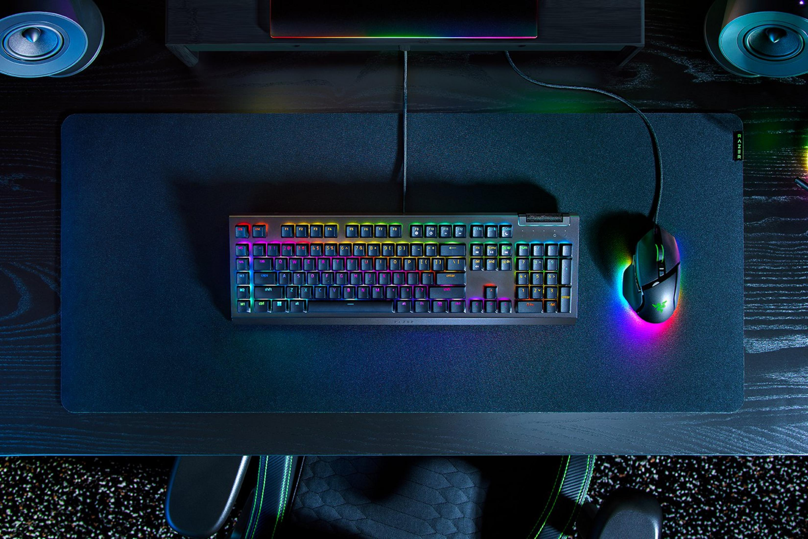 Un'impostazione di gioco con tastiera, mouse e altoparlanti su una scrivania. La tastiera e il mouse hanno luci colorate.