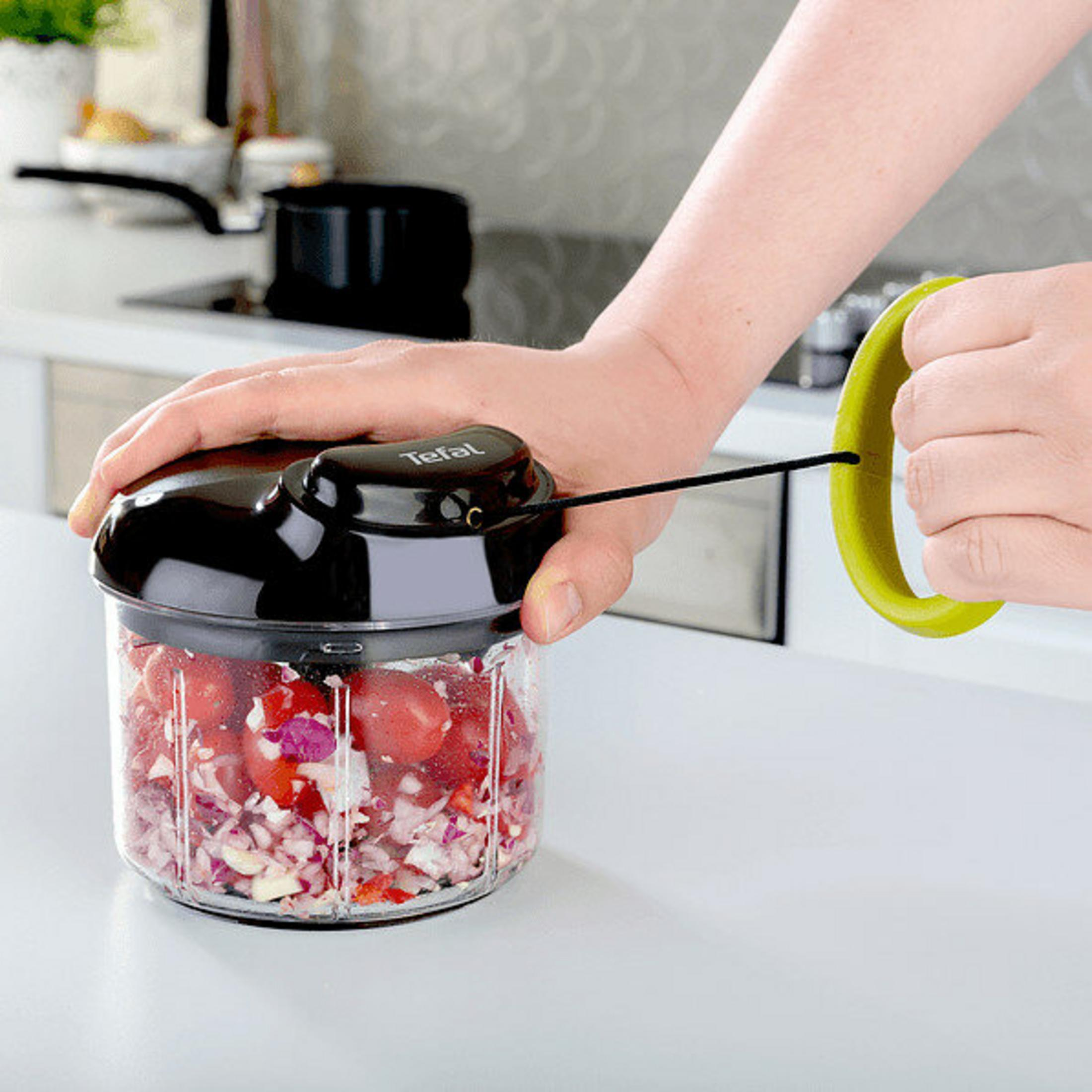 Osoba używa rozdrabniacza do żywności Tefal. Zawiera posiekane pomidory i cebulę. Zielony uchwyt w drugiej dłoni.
