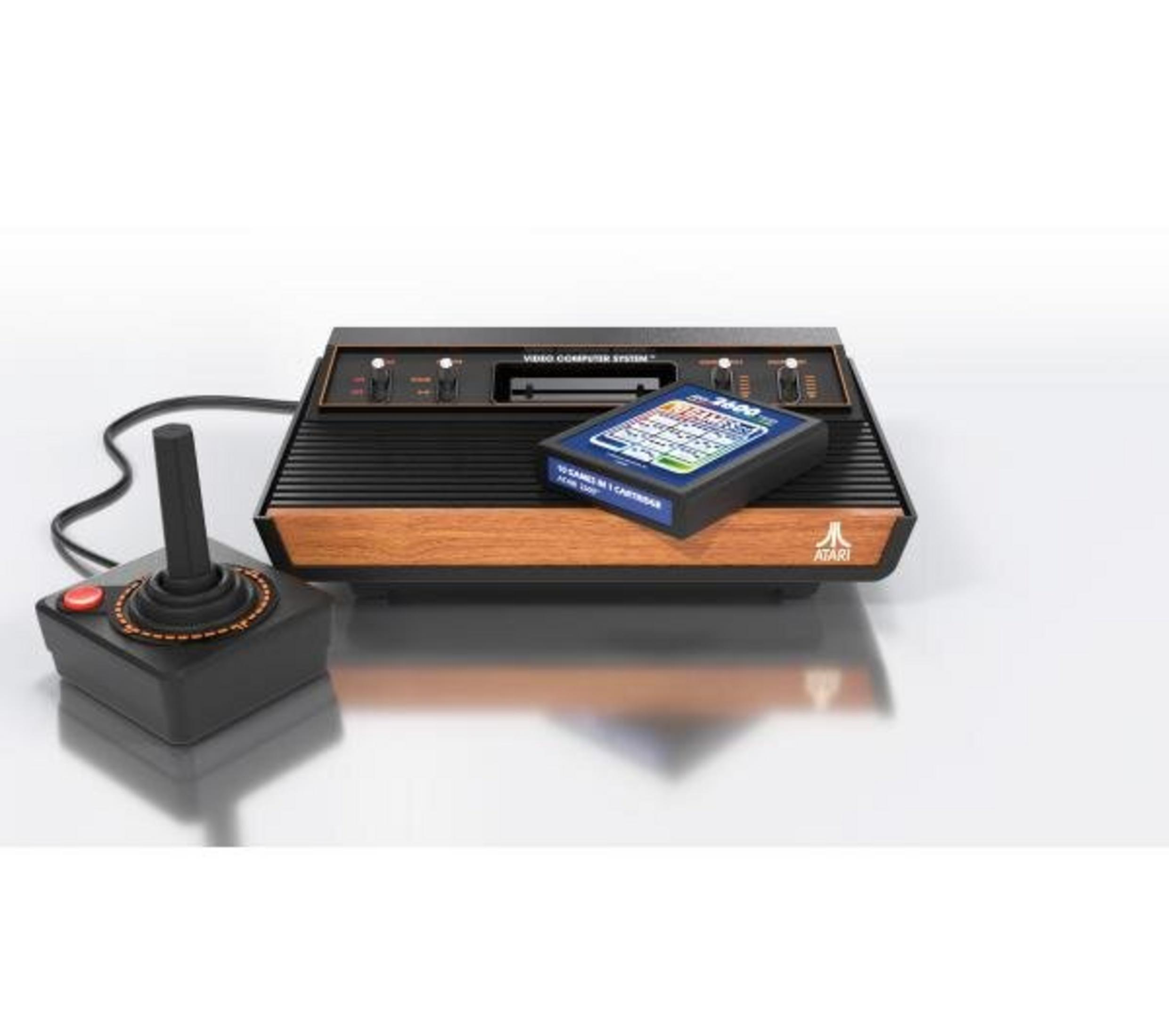 Konsola do gier Atari z joystickiem i kartridżem na białej powierzchni.