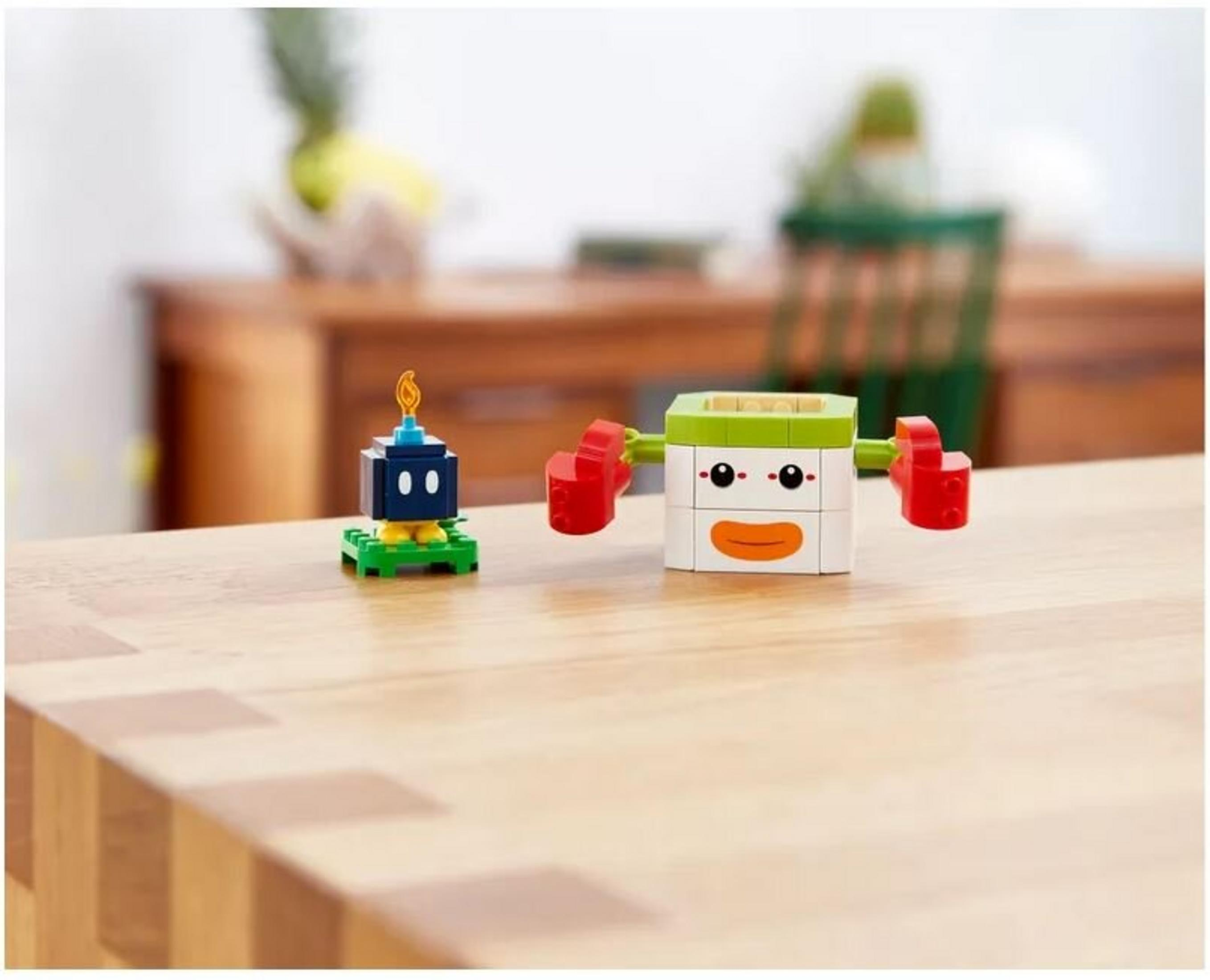LEGO-Figuren auf einem Holztisch. Eine schwarze Bombenfigur mit Flamme und eine weiße Figur mit roten Armen sind sichtbar.