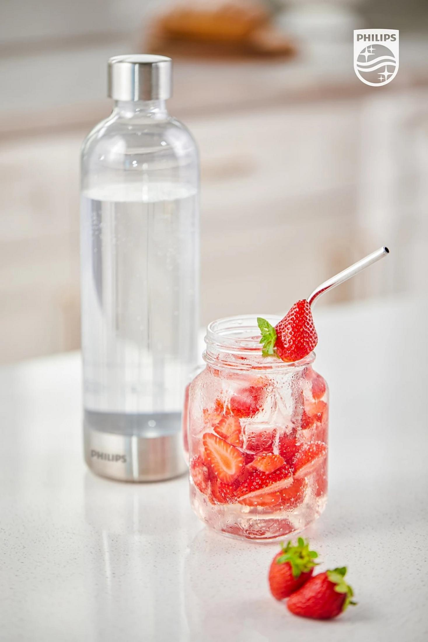 Una bottiglia d'acqua trasparente e un barattolo pieno d'acqua alle fragole. Fragole e foglie di menta guarniscono la bevanda. Un logo Philips è visibile.