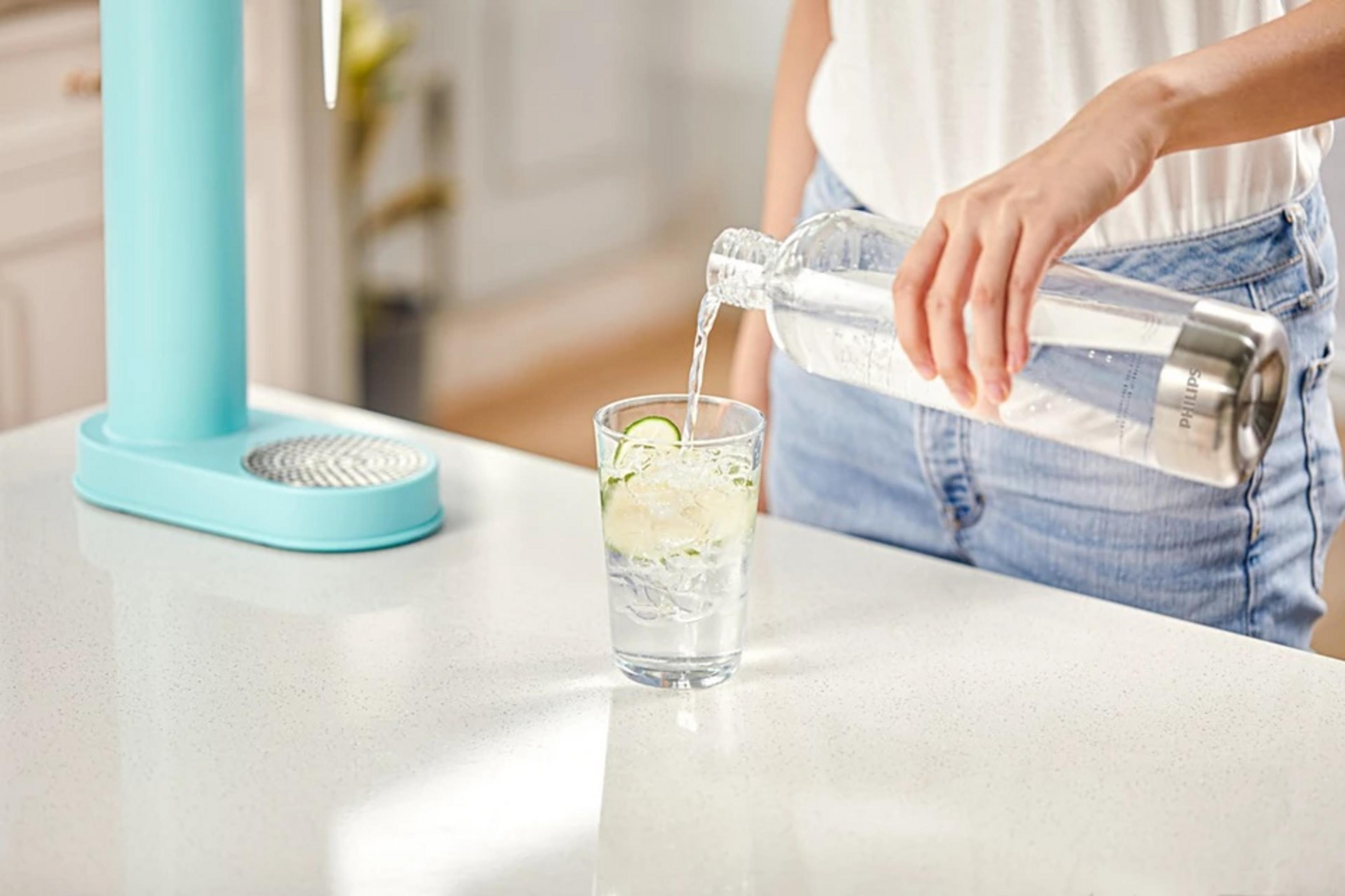 Una persona versa acqua da una bottiglia in un bicchiere con ghiaccio e fette di lime. A sinistra c'è un distributore d'acqua blu.