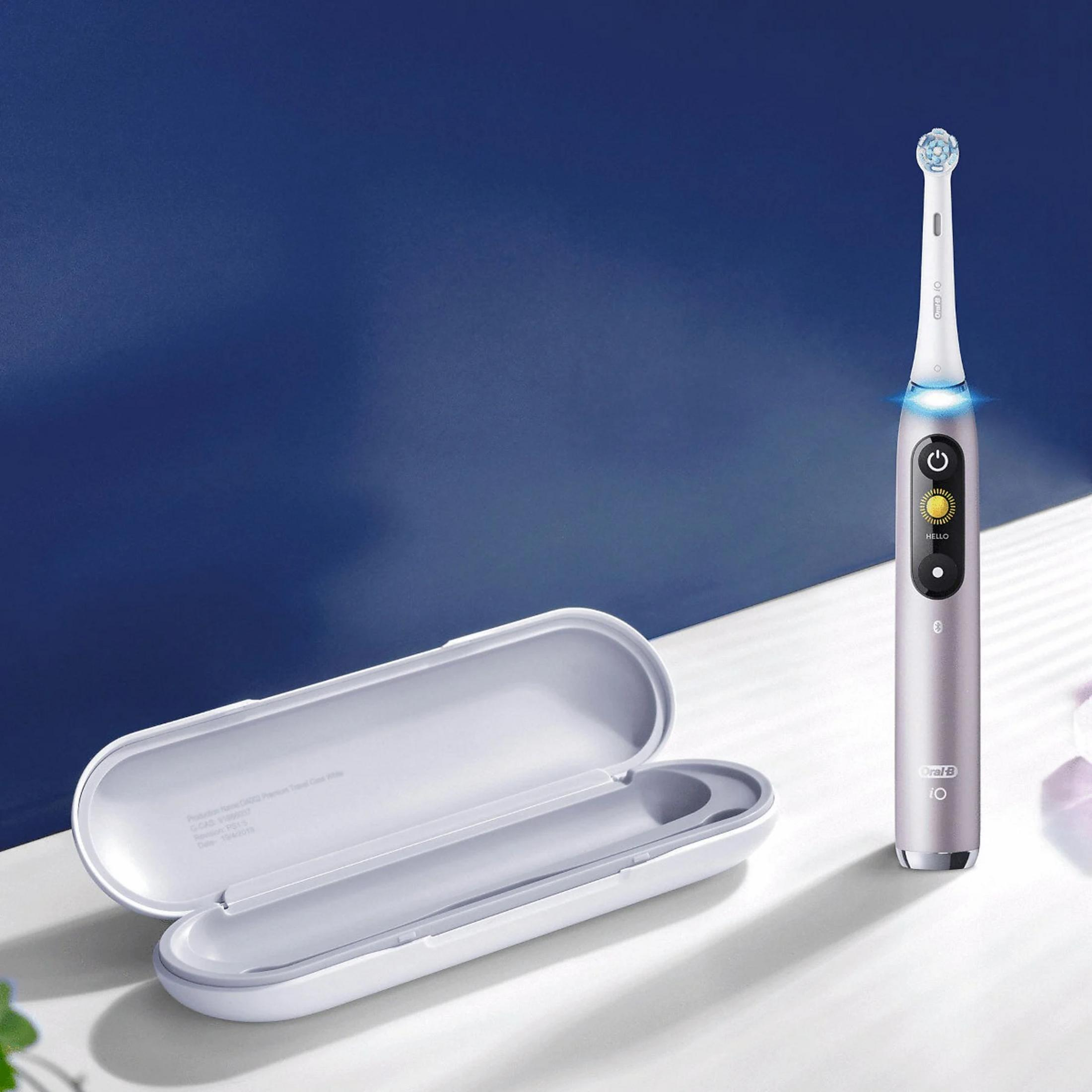 A gray electric toothbrush, case, and blue background are in the image. The toothbrush has a white head.