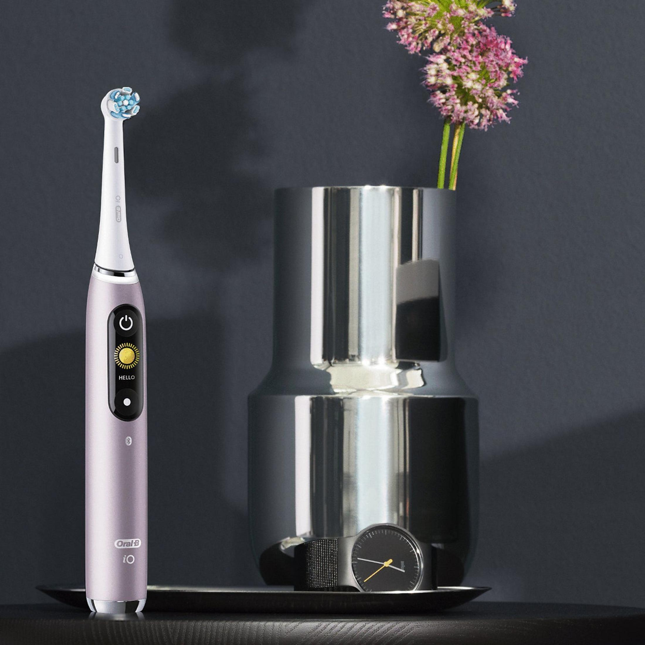 A toothbrush, vase with flowers, and a watch on a tray. The toothbrush is purple, the vase silver, and the watch black.