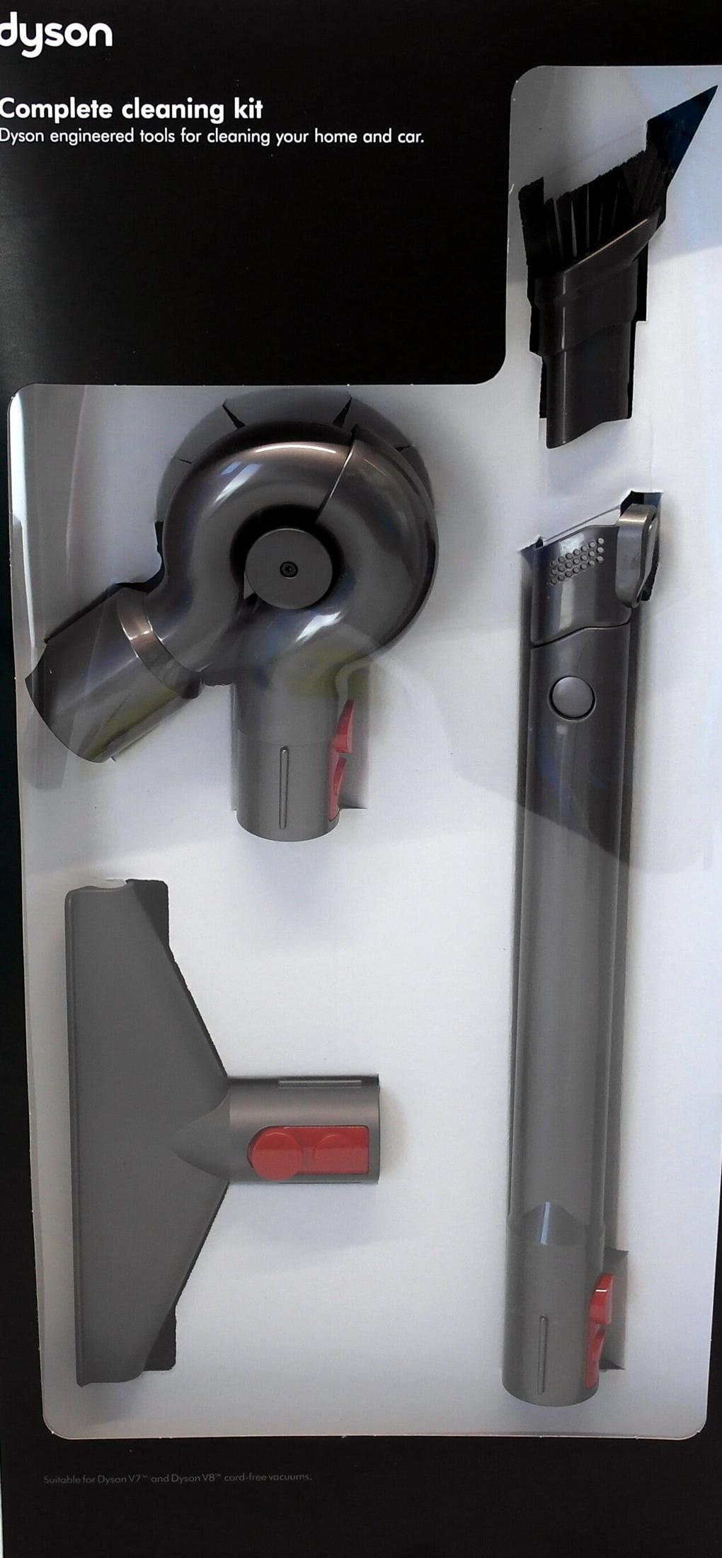 Kit de nettoyage Dyson avec divers accessoires d'aspirateur gris et boutons de déverrouillage rouges, disposés dans un plateau en plastique blanc.
