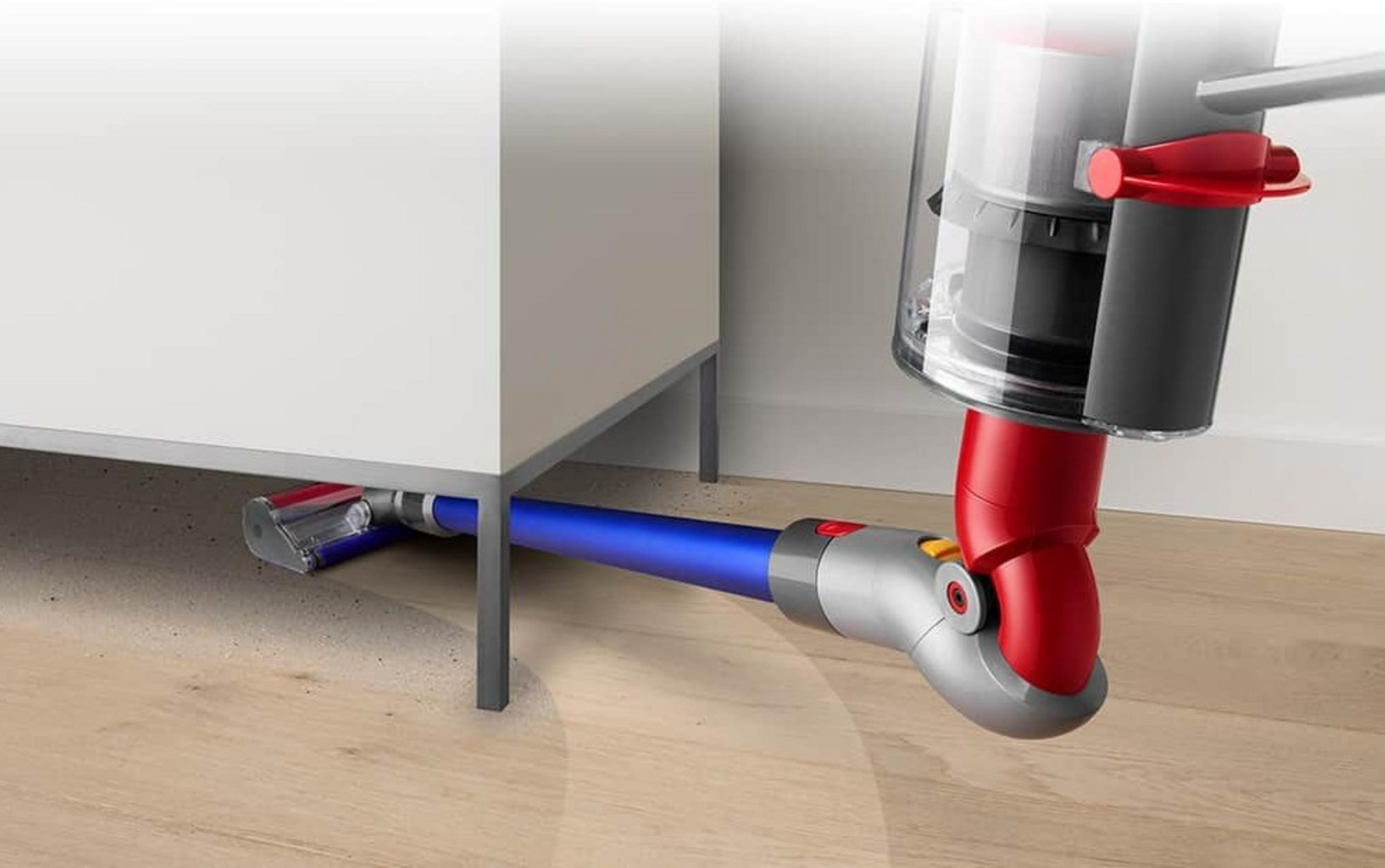 Ein rot-blauer Staubsauger reinigt unter einem weißen Schrank auf einem Holzboden.