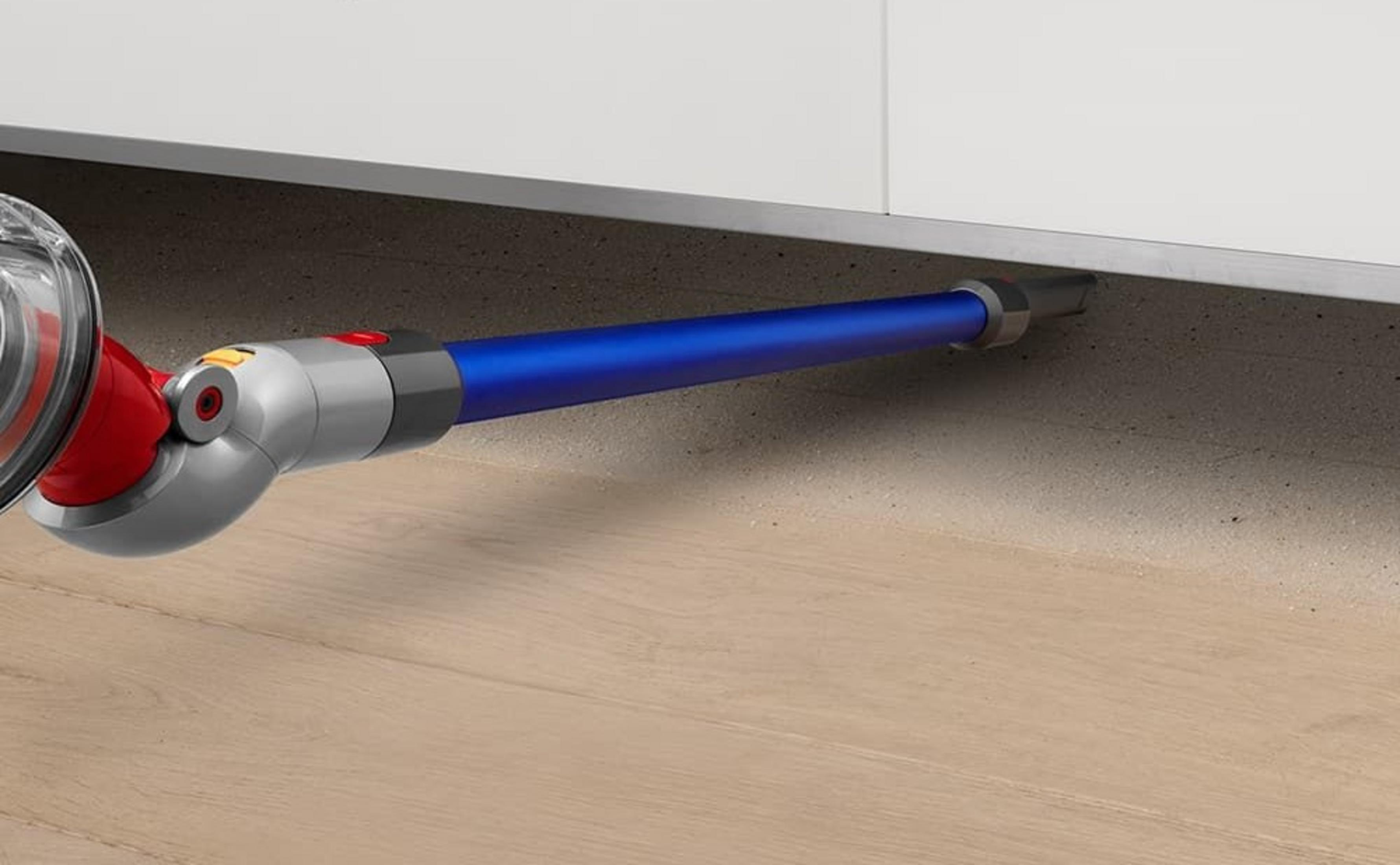 Eine blaue Staubsaugerdüse reinigt den Raum in der Nähe eines weißen Schranks auf einem Holzboden.