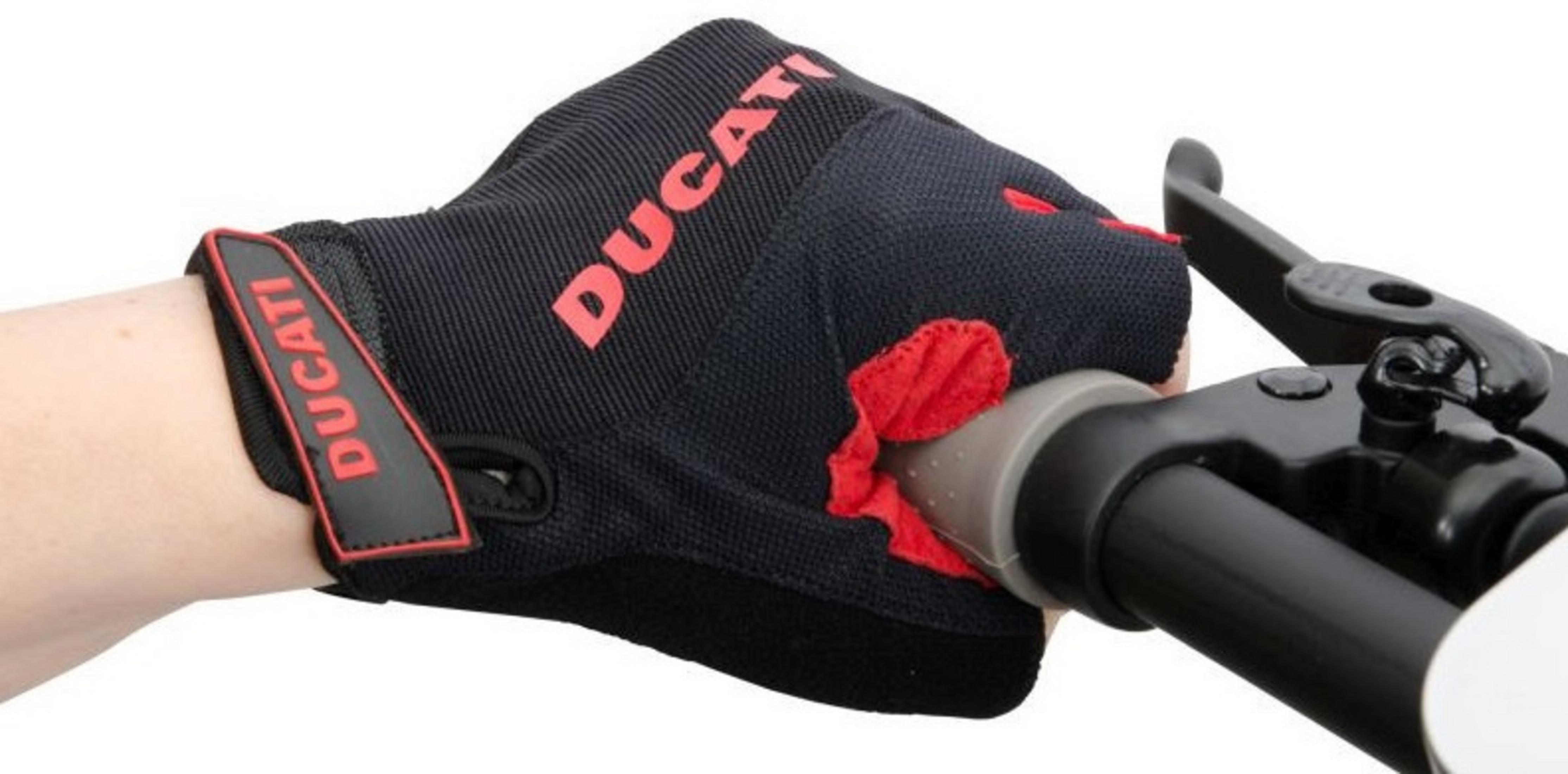 Una mano con un guanto Ducati nero afferra un manubrio. Logo Ducati rosso. Tessuto rosso sul palmo. Leva del freno nera.