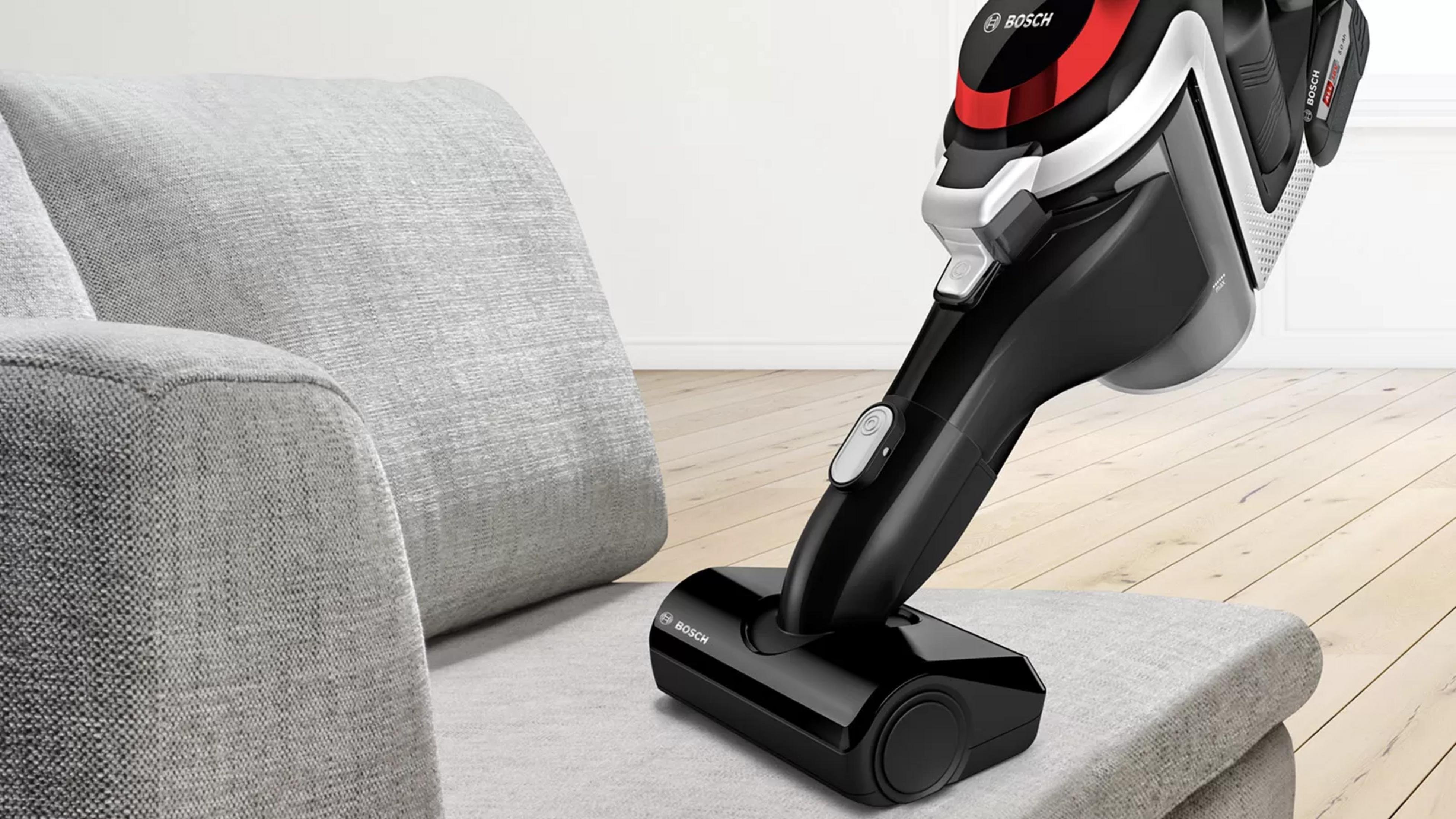 Una aspiradora Bosch negra y roja está sobre un sofá gris. El fondo es un suelo de madera y un sofá gris.