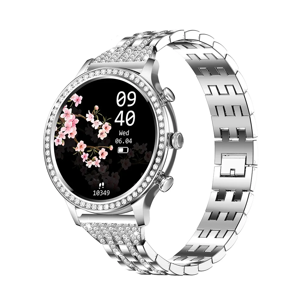 Srebrny smartwatch z czarnym ekranem wyświetlającym czas i kwiatowy wzór. Zegarek ma diamentową ramkę i pasek.