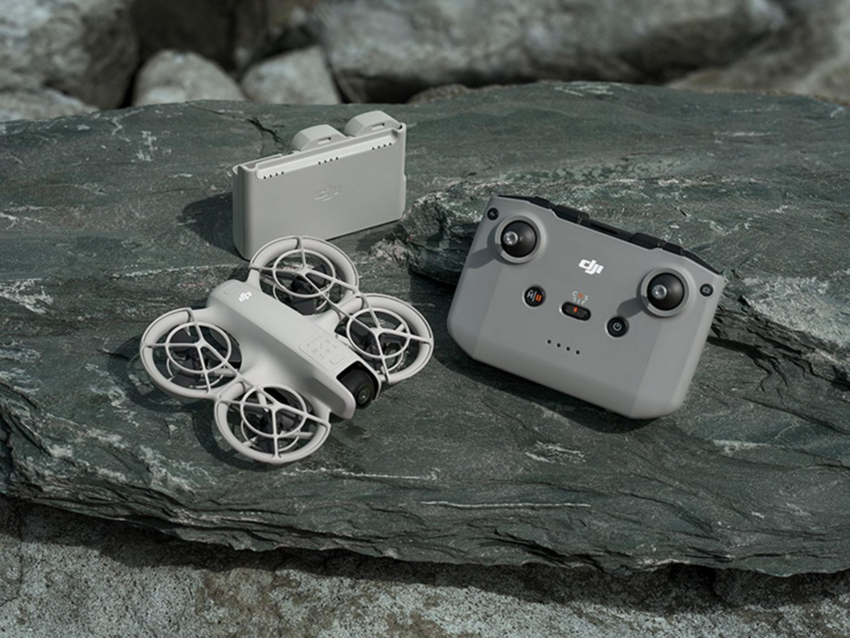 Un dron, un controlador y una funda de batería están sobre una roca. El dron es blanco, el controlador gris y la funda gris.