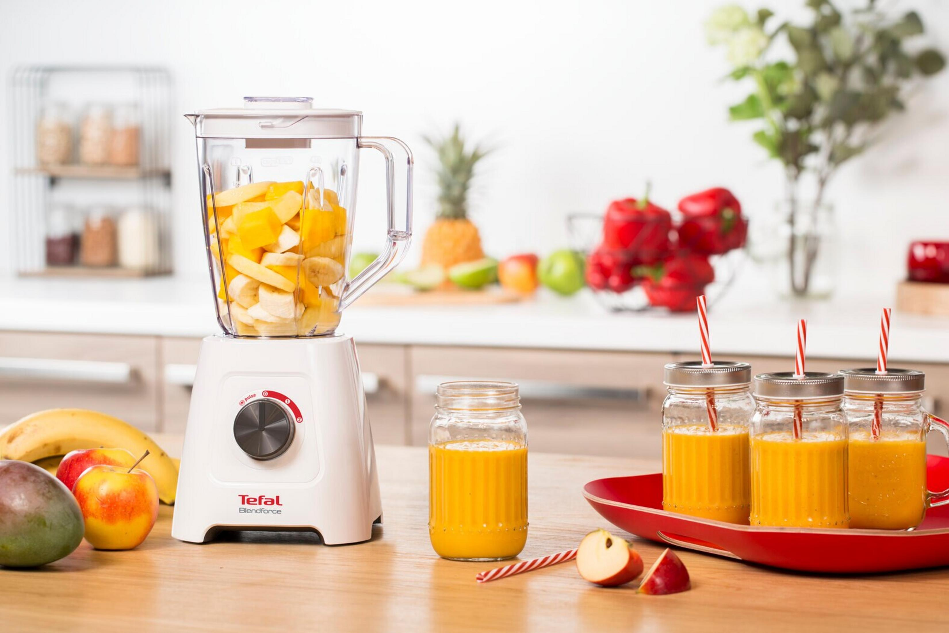 Ein Mixer mit Früchten, Smoothie-Gläsern und einem Tablett. Zu den Früchten gehören Äpfel, Bananen, Mangos und Ananas.