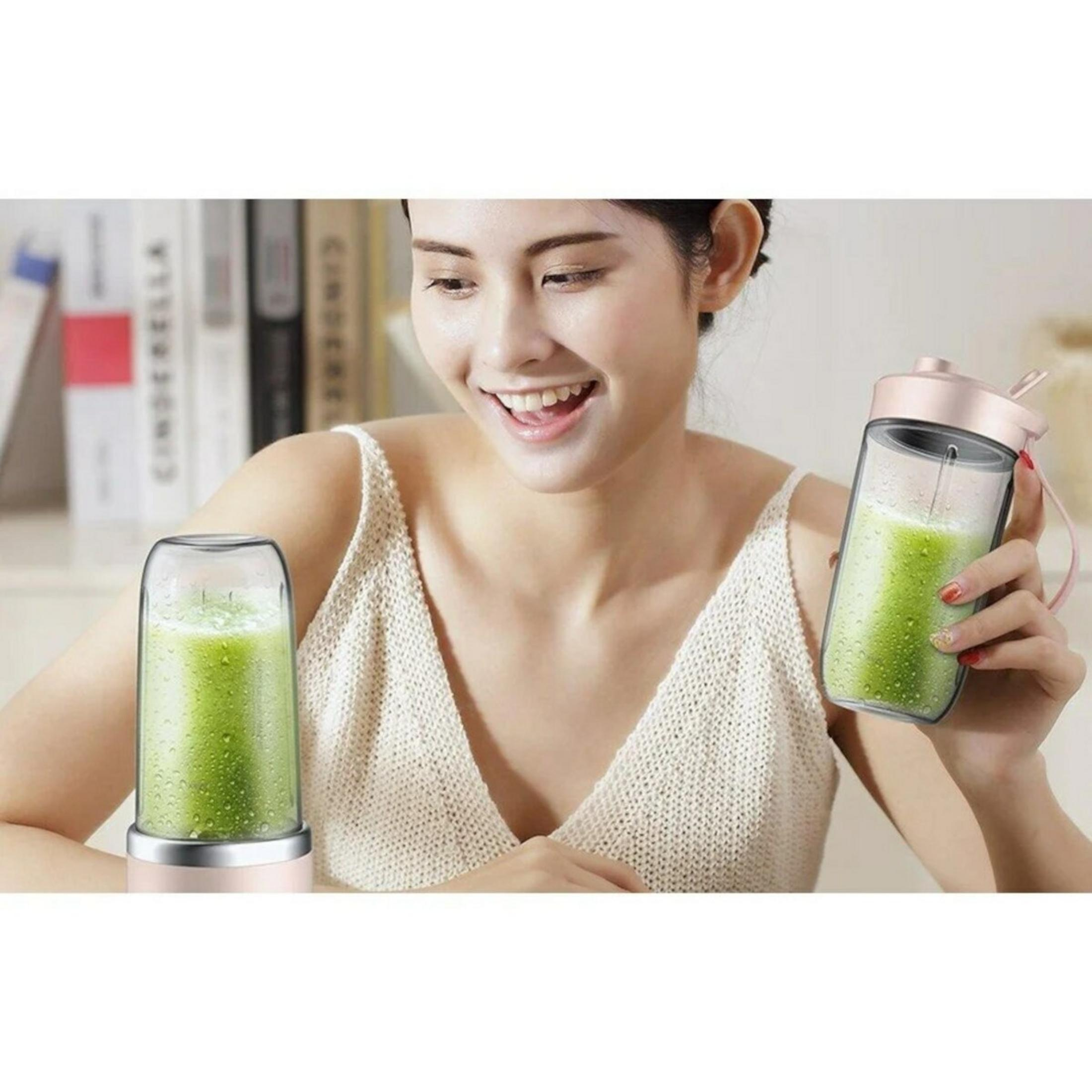 Una donna sorride, tenendo in mano un bicchiere di frullato. Un altro bicchiere è su un frullatore. Entrambi sono pieni di liquido verde.