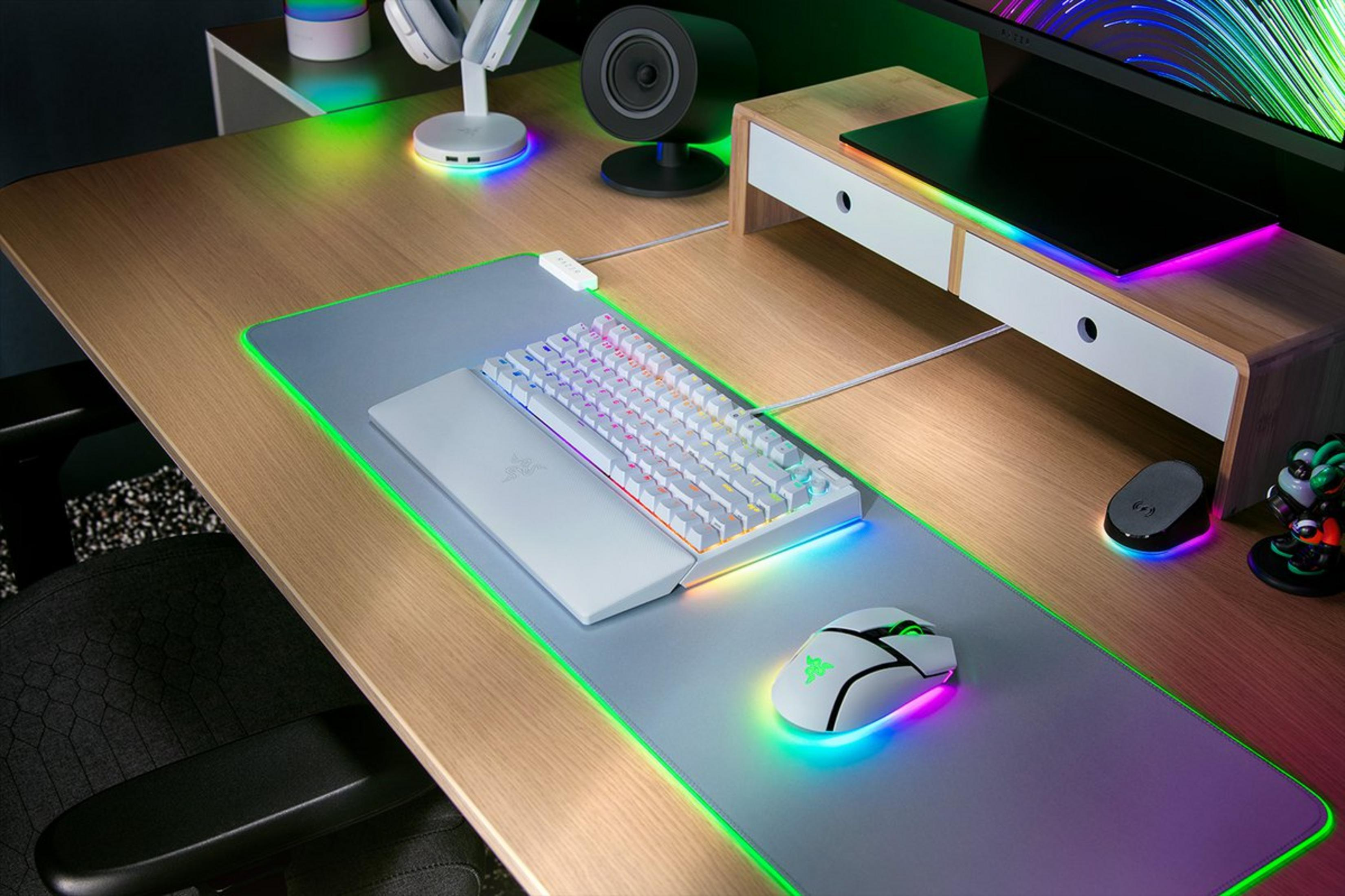 Een bureau-opstelling met toetsenbord, muis en muismat. Allemaal hebben RGB-verlichting. Een monitor staat op een houten standaard.