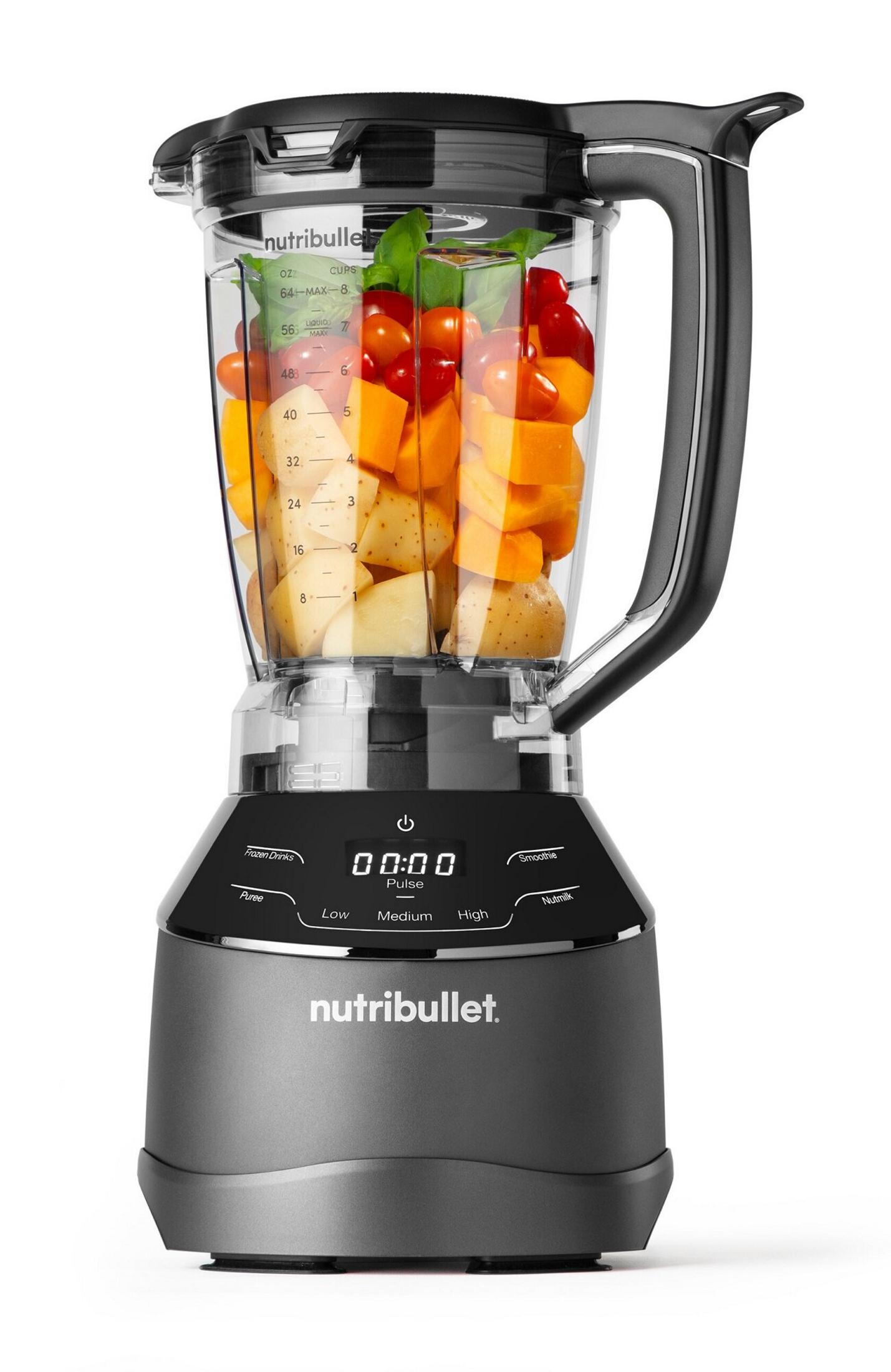 Blender Nutribullet wypełniony warzywami, takimi jak pomidory, dynia, ziemniaki i bazylia. Blender jest czarny i szary.