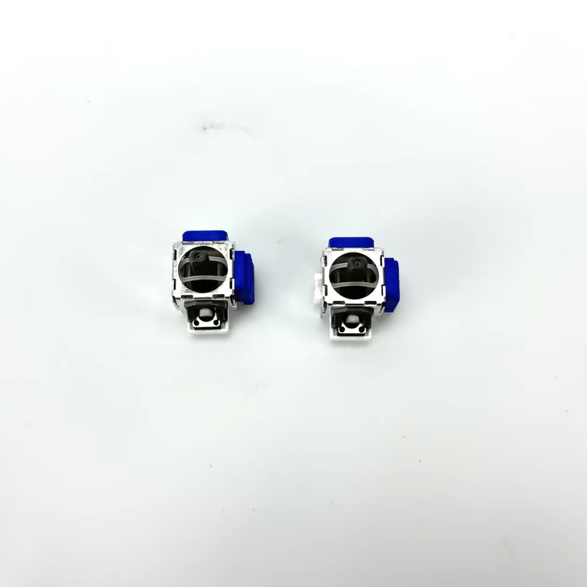 Dwa elementy elektroniczne na białej powierzchni. Mają niebieską górę i są srebrne. Tło jest białe.