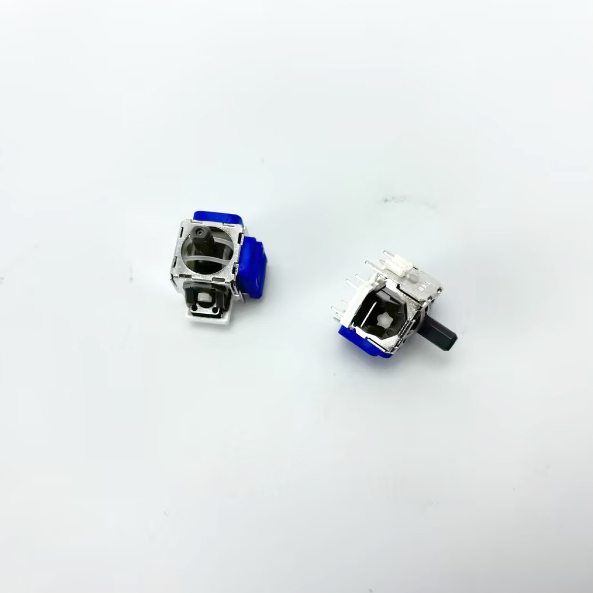 Dwa srebrne i niebieskie moduły joysticka na białej powierzchni. Jeden ma czarny drążek.